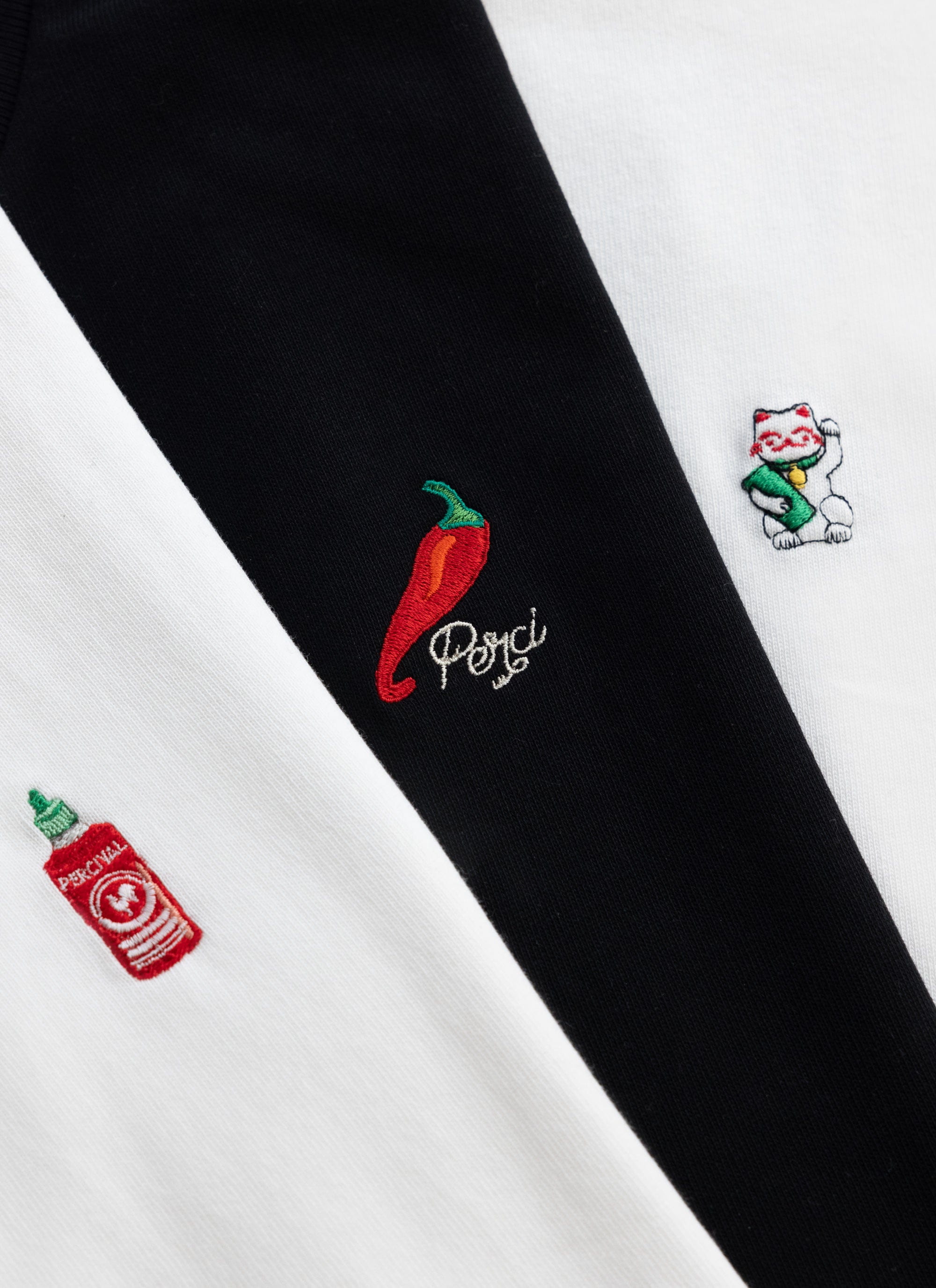 A close-up of the unique embroidery from the Percival t-shirt collection, including a lucky cat, chilli and hot sauce.