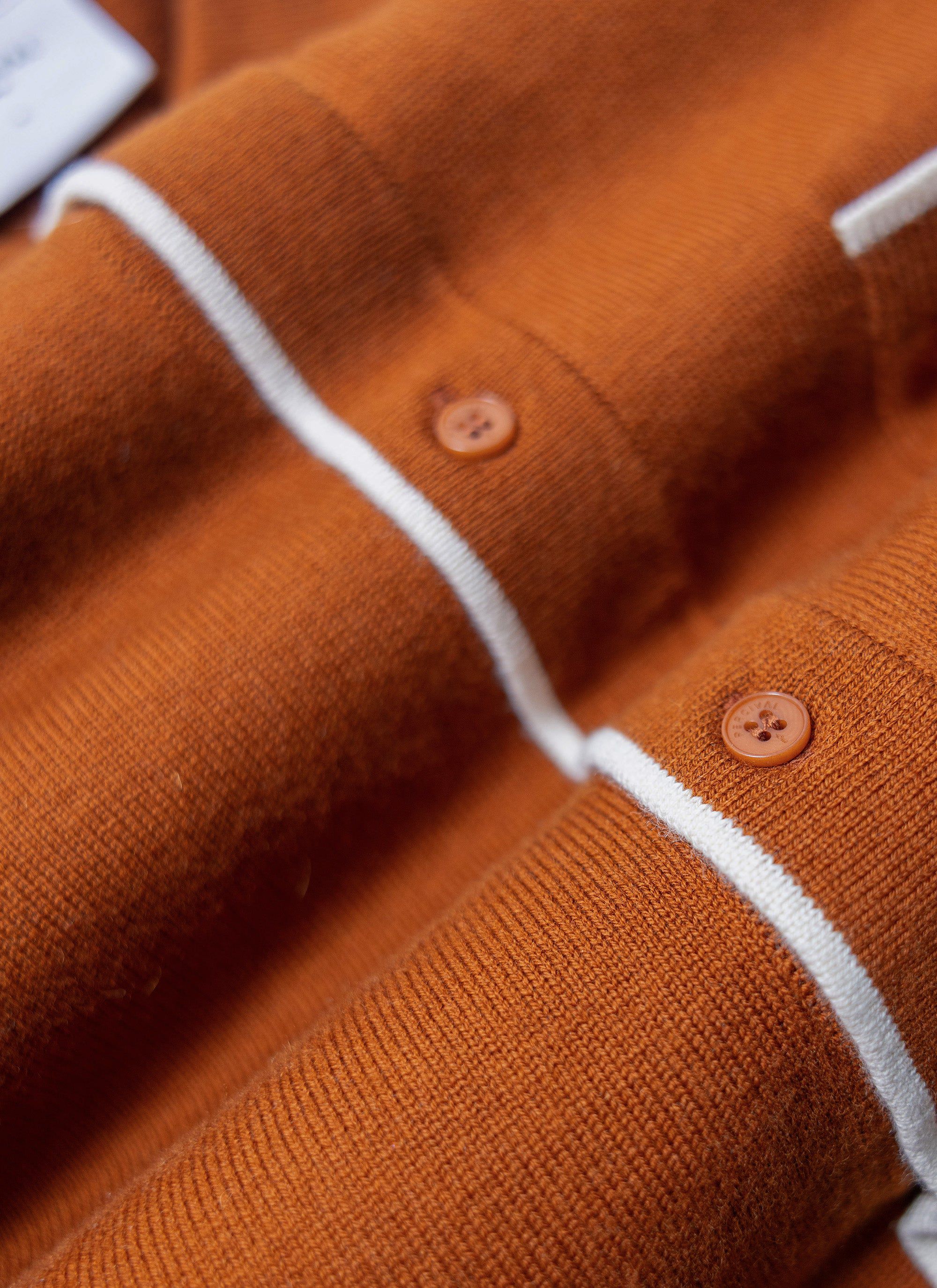 A close-up of the Percival Contrast Trim Shirt in rust, detailing the wool-blend knit, white trim and branded buttons.