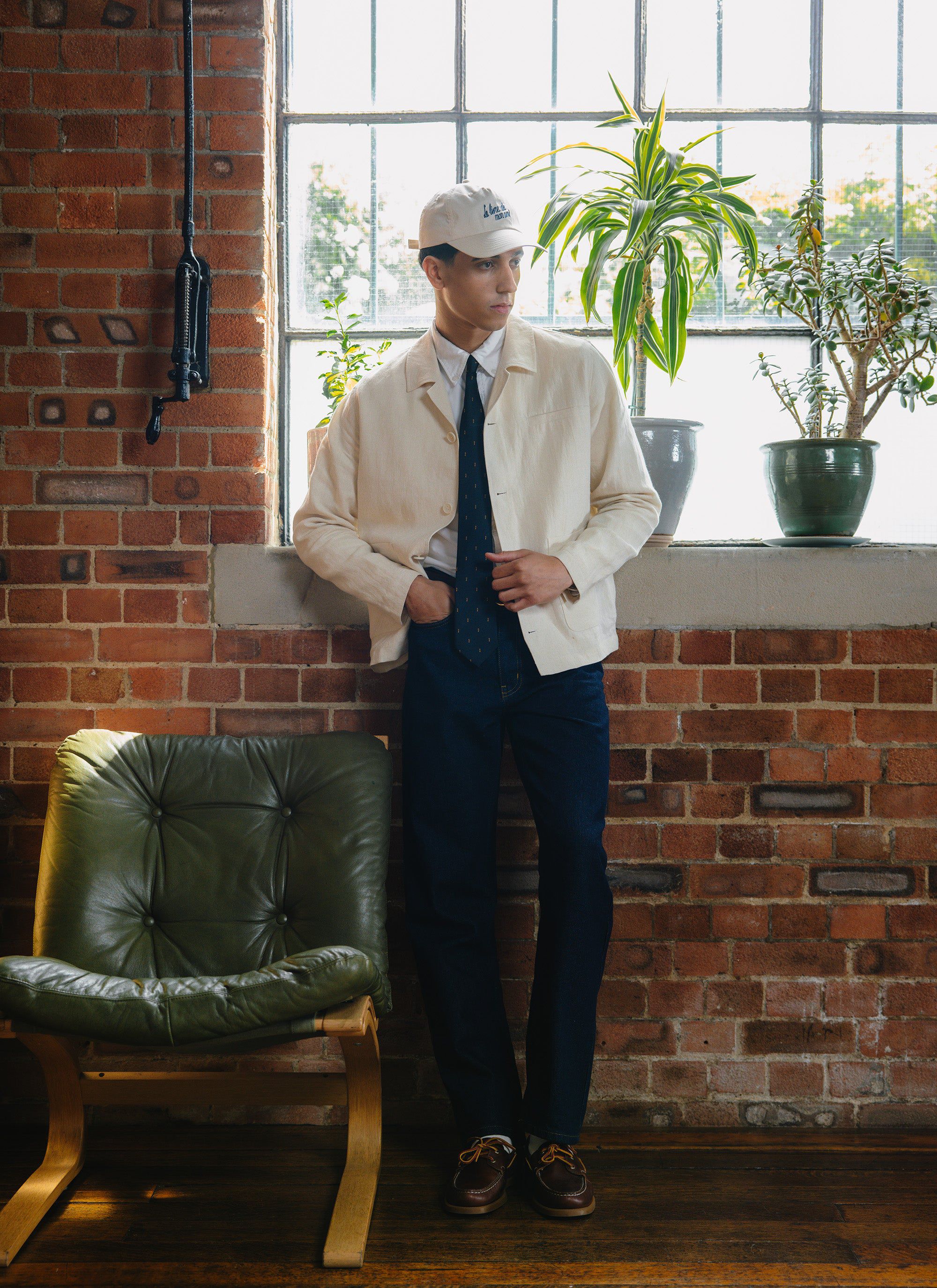 A man models the Percival Relaxed Linen Overshirt in stone, paired with dark jeans and a tie in a sunlit loft.