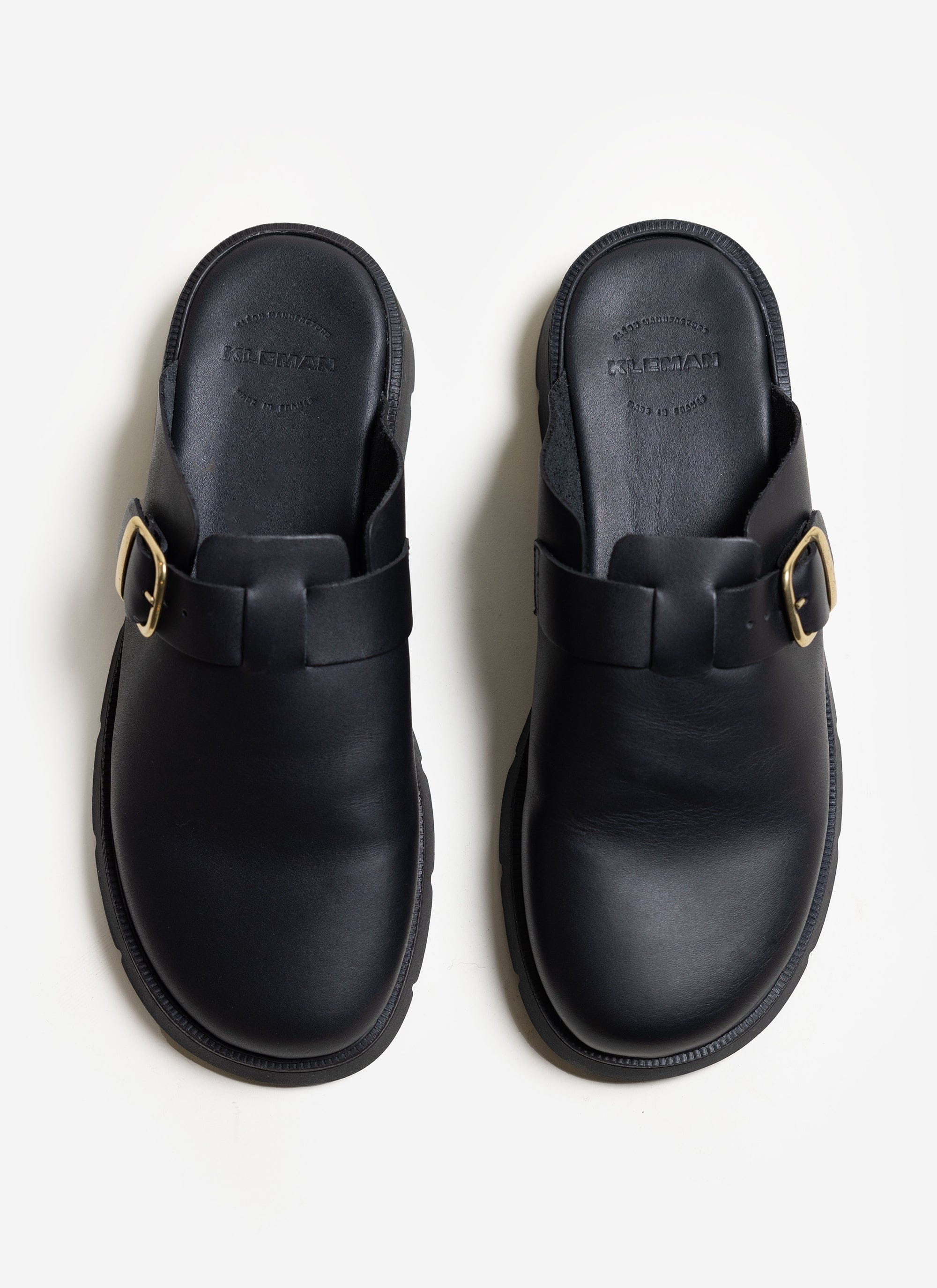 A top-down view of the black leather Kleman Pacha sandals with gold buckles, available at Percival.