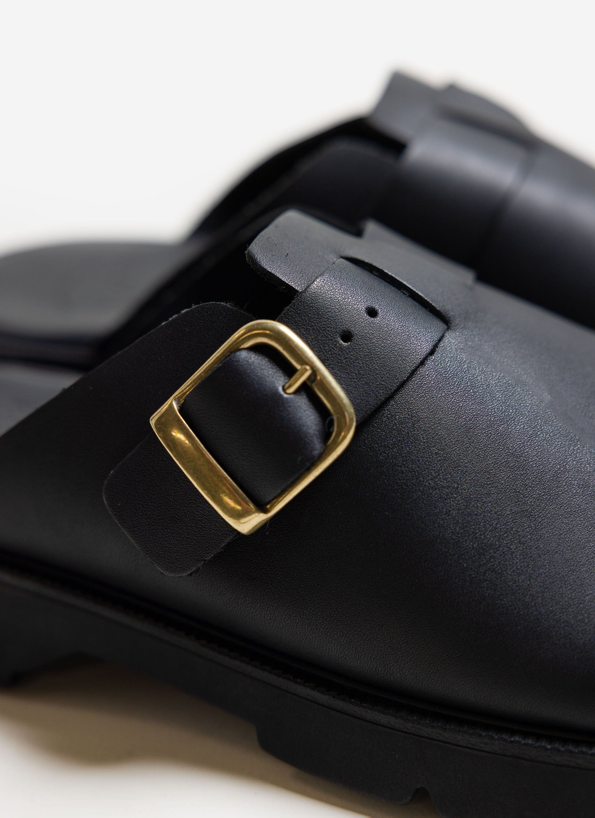 A close-up of the black leather Kleman Pacha Sandals from Percival, showing the detailed gold buckle.