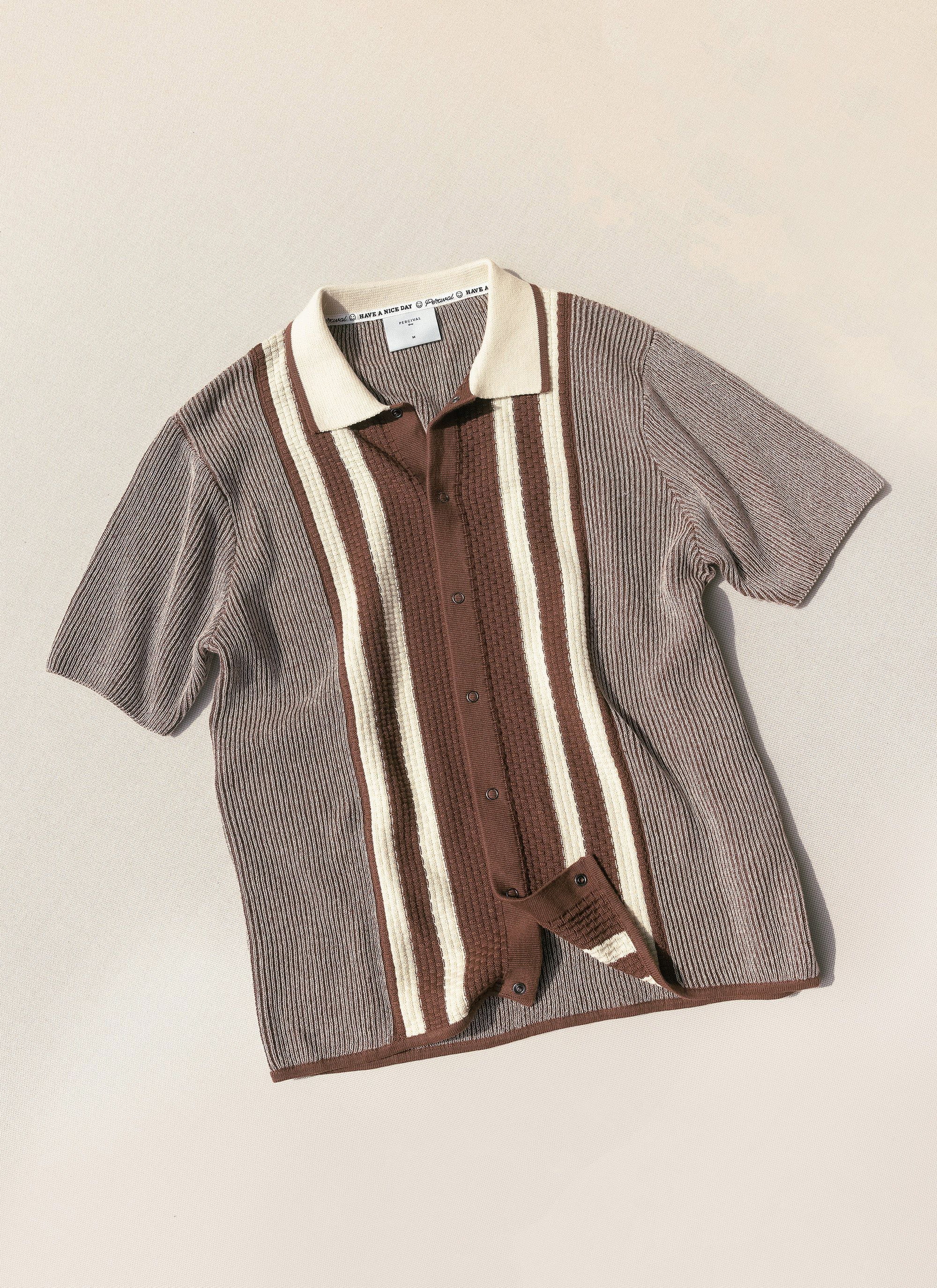A flat lay of the Percival Teramo Knitted Polo Shirt in ecru, featuring a textured knit and bold brown vertical stripes.