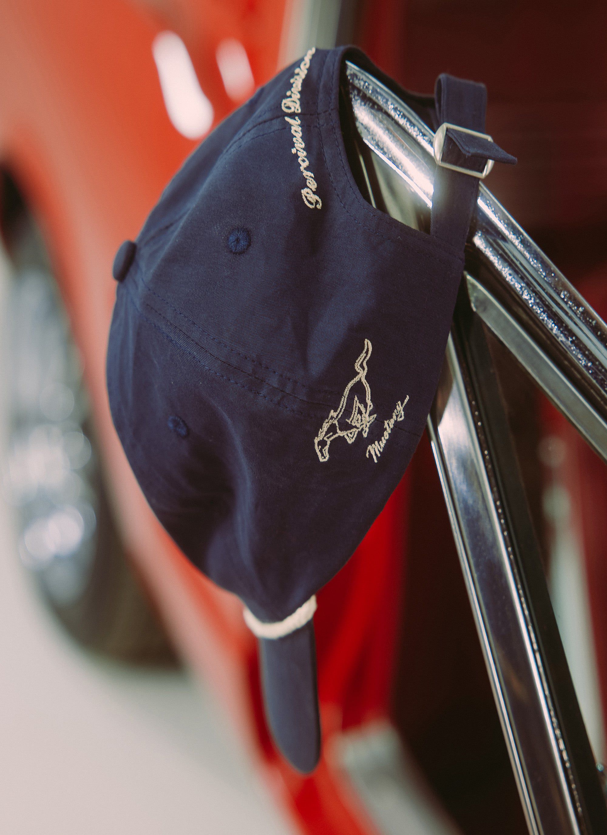 A close-up of the navy Percival x Ford trucker cap showing the 'Mustang' and 'Percival Division' embroidery detail.