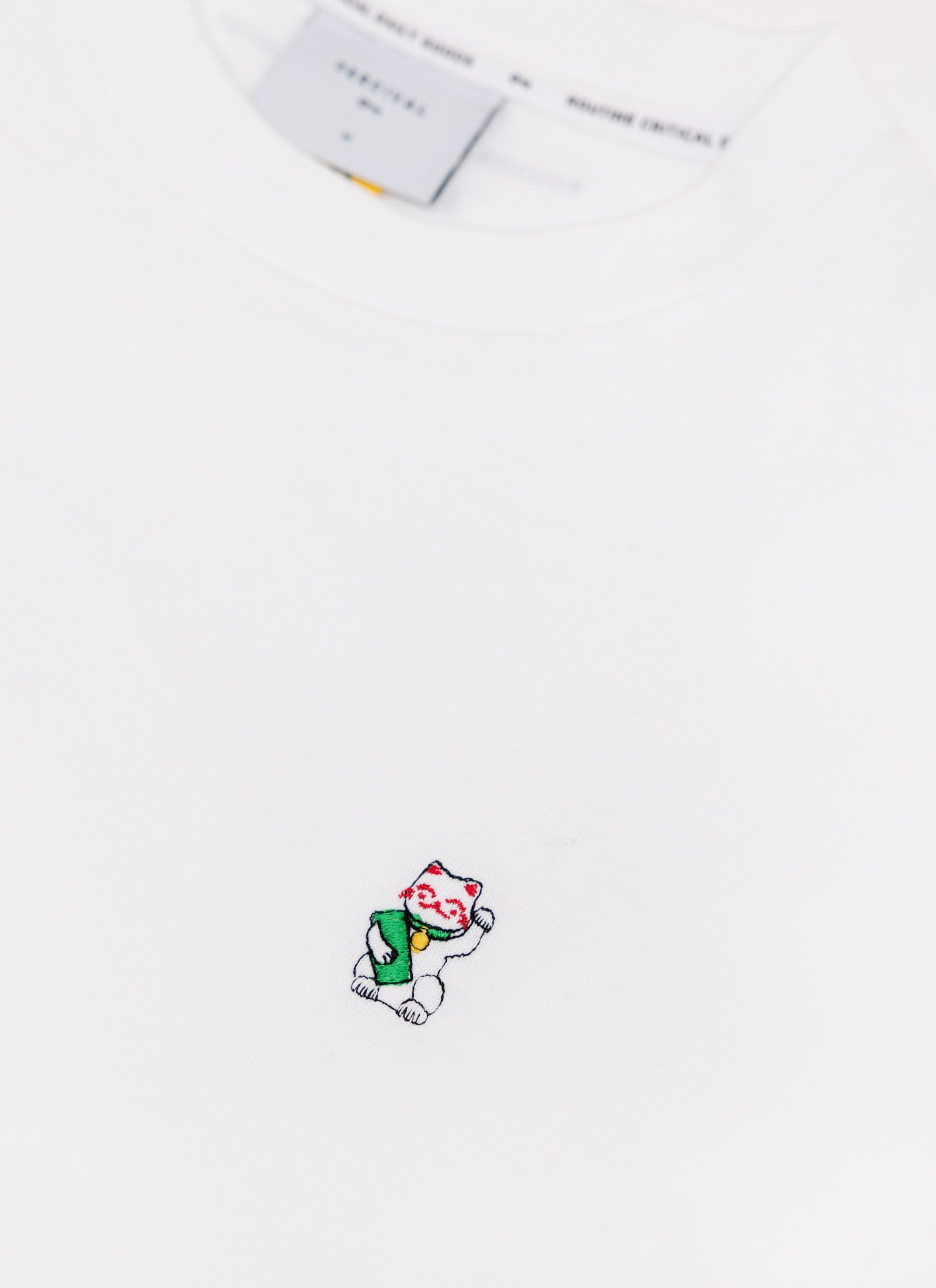 A close-up of the Percival Loyalty T Shirt in white, showing the embroidered Lucky Cat detail on the chest.
