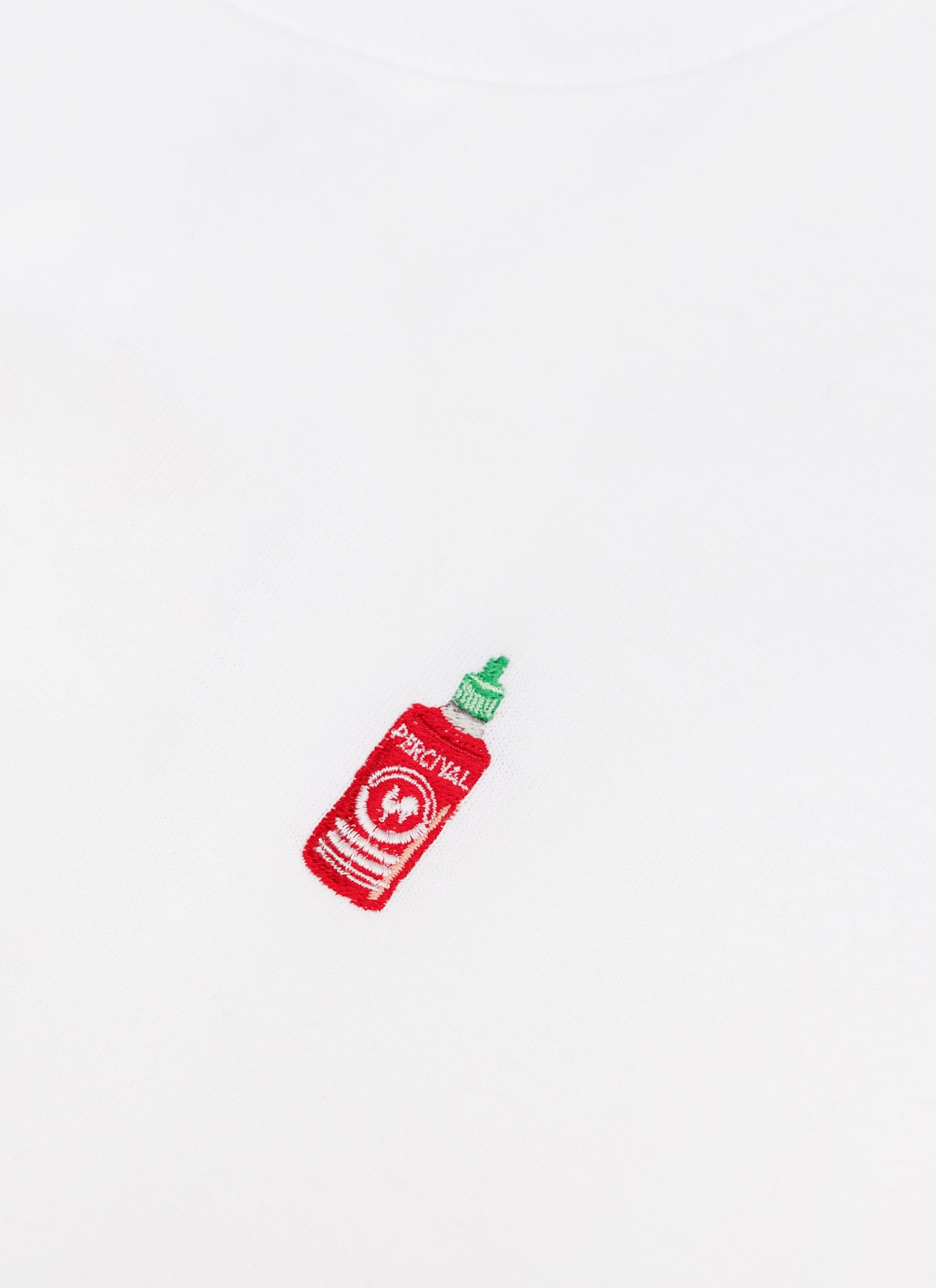 A close-up of the hot sauce bottle embroidery on the chest of the white Percival Loyalty T-shirt.
