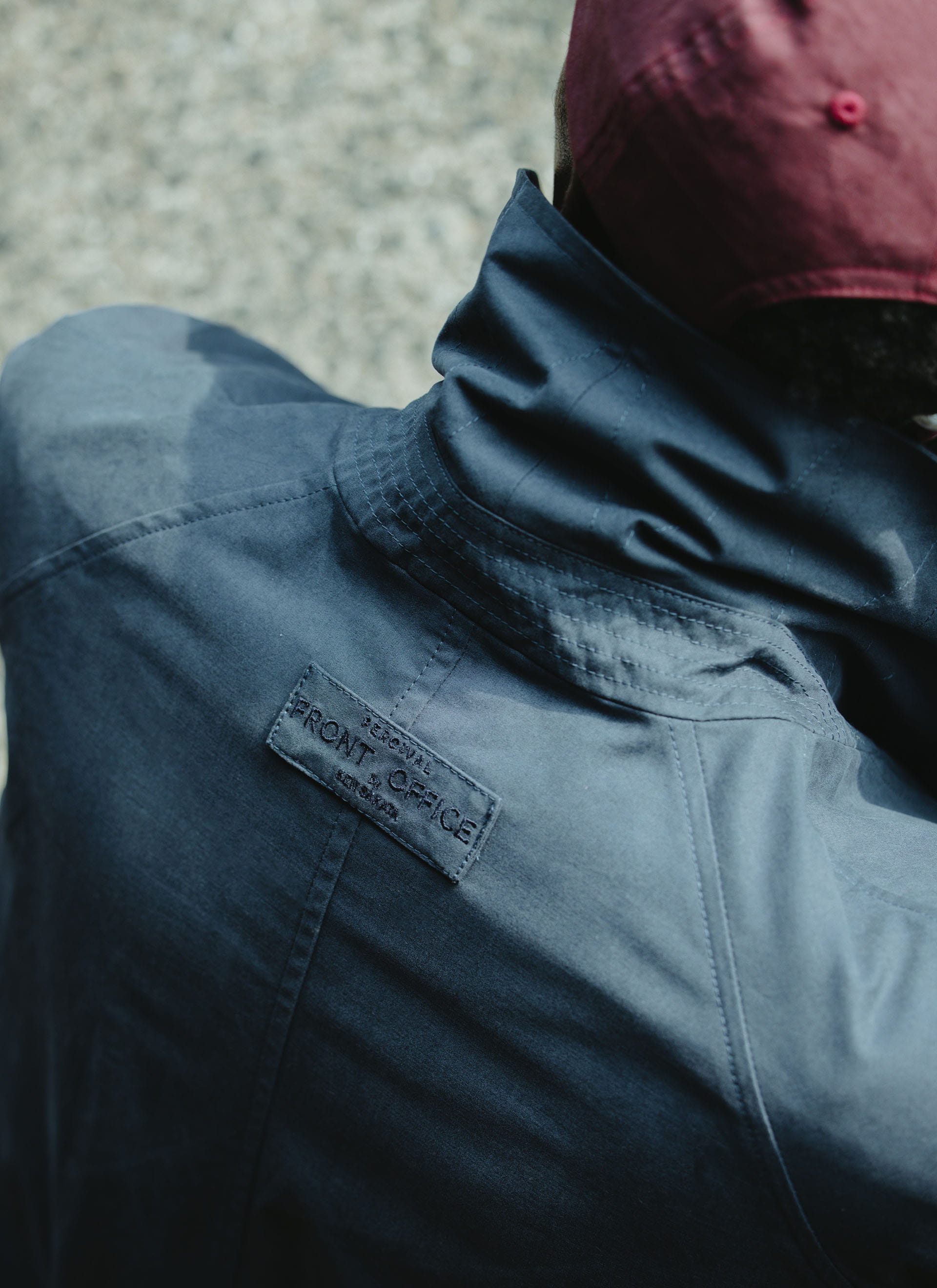 Close-up of the embroidered collaboration tab on the navy Percival x Front Office peached cotton Mac trench coat.