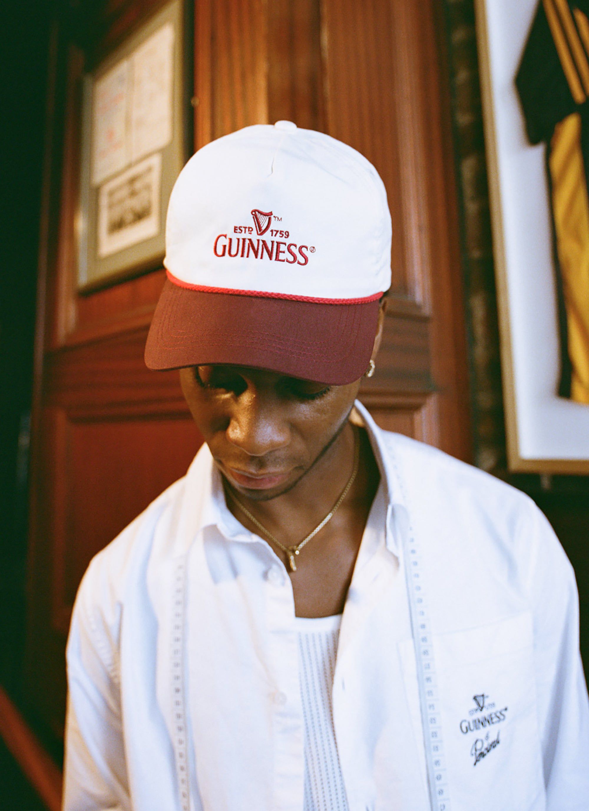 A model wears the white Guinness x Percival boxy shirt, featuring the embroidered logo, paired with a Guinness cap.