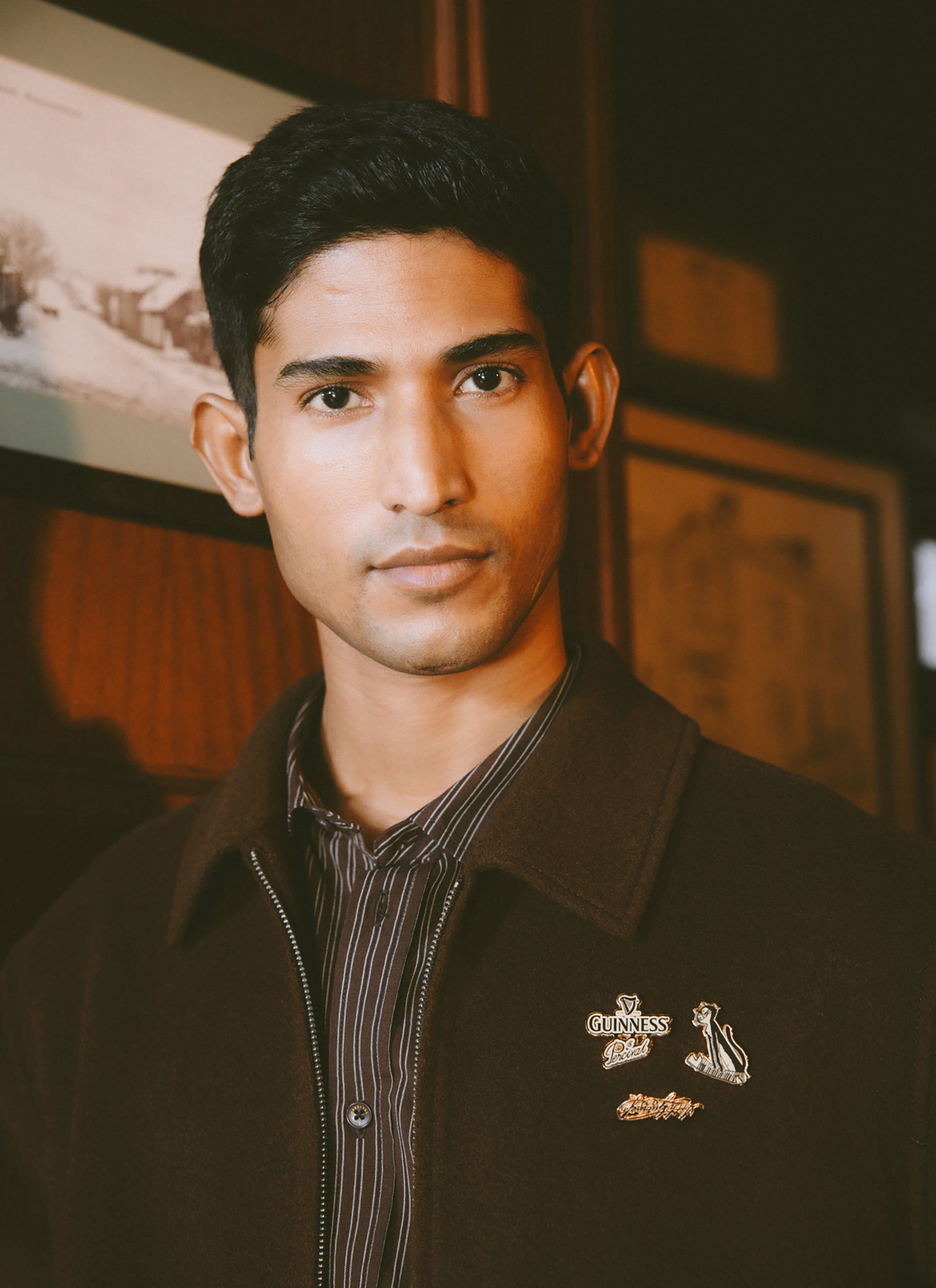 A close-up of a man modelling the Guinness x Percival wool jacket in espresso, showing the collaboration pin badges.