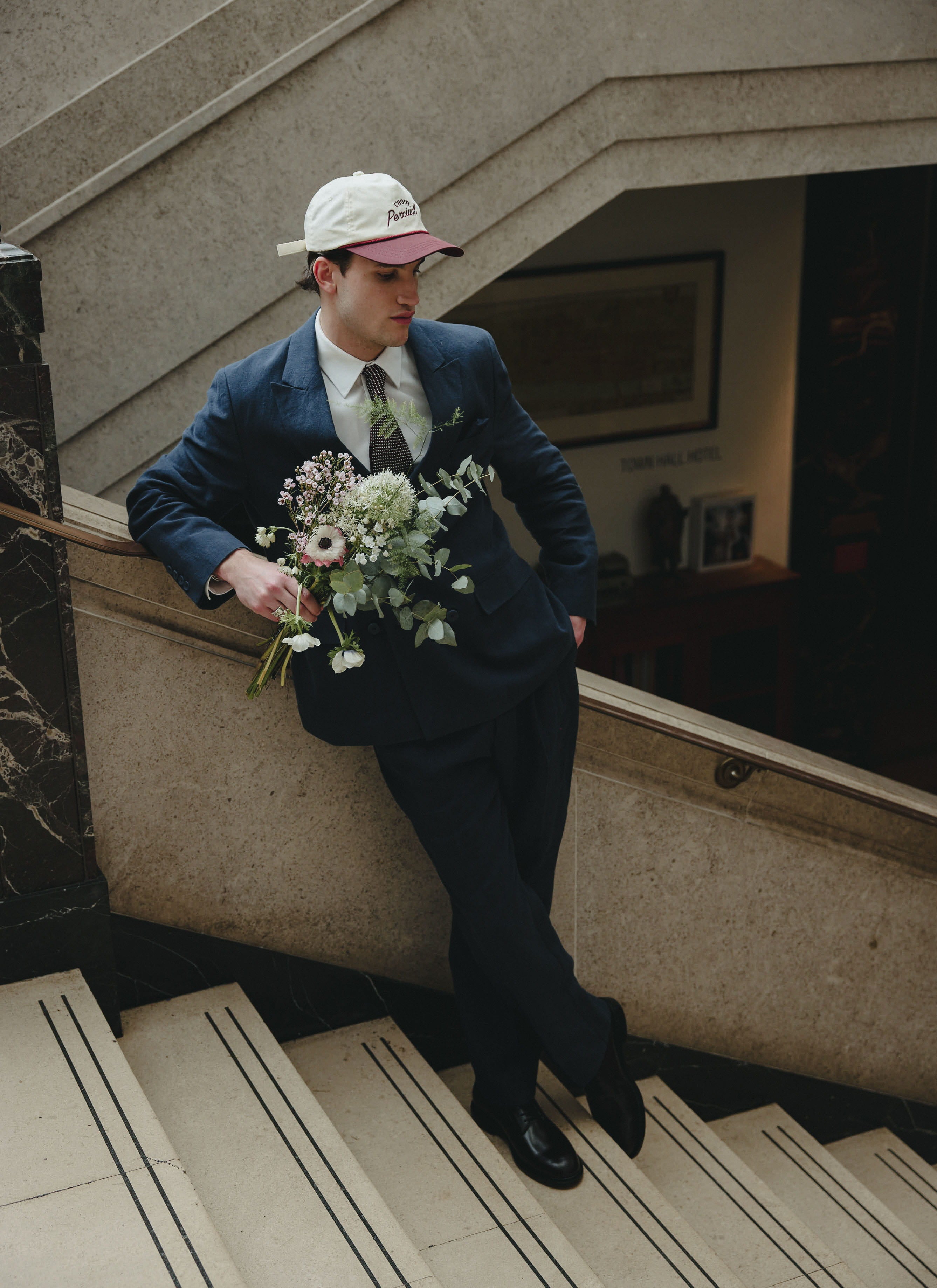 Model wearing the navy Percival Clifton linen double-breasted blazer and trousers, holding a bouquet of flowers.