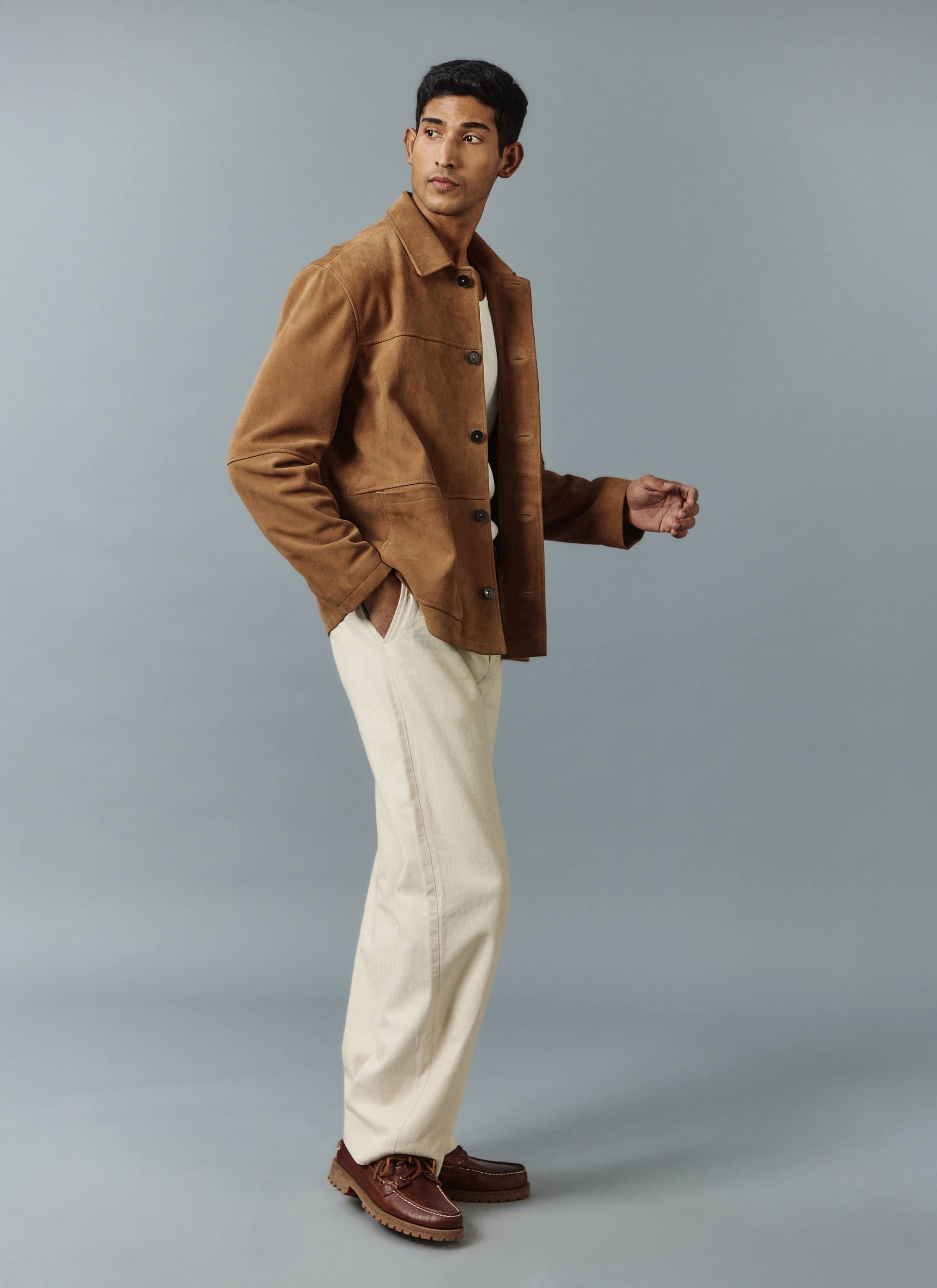 A model wears the tan suede Afterward Chore Jacket from Percival with cream trousers and a white t-shirt.