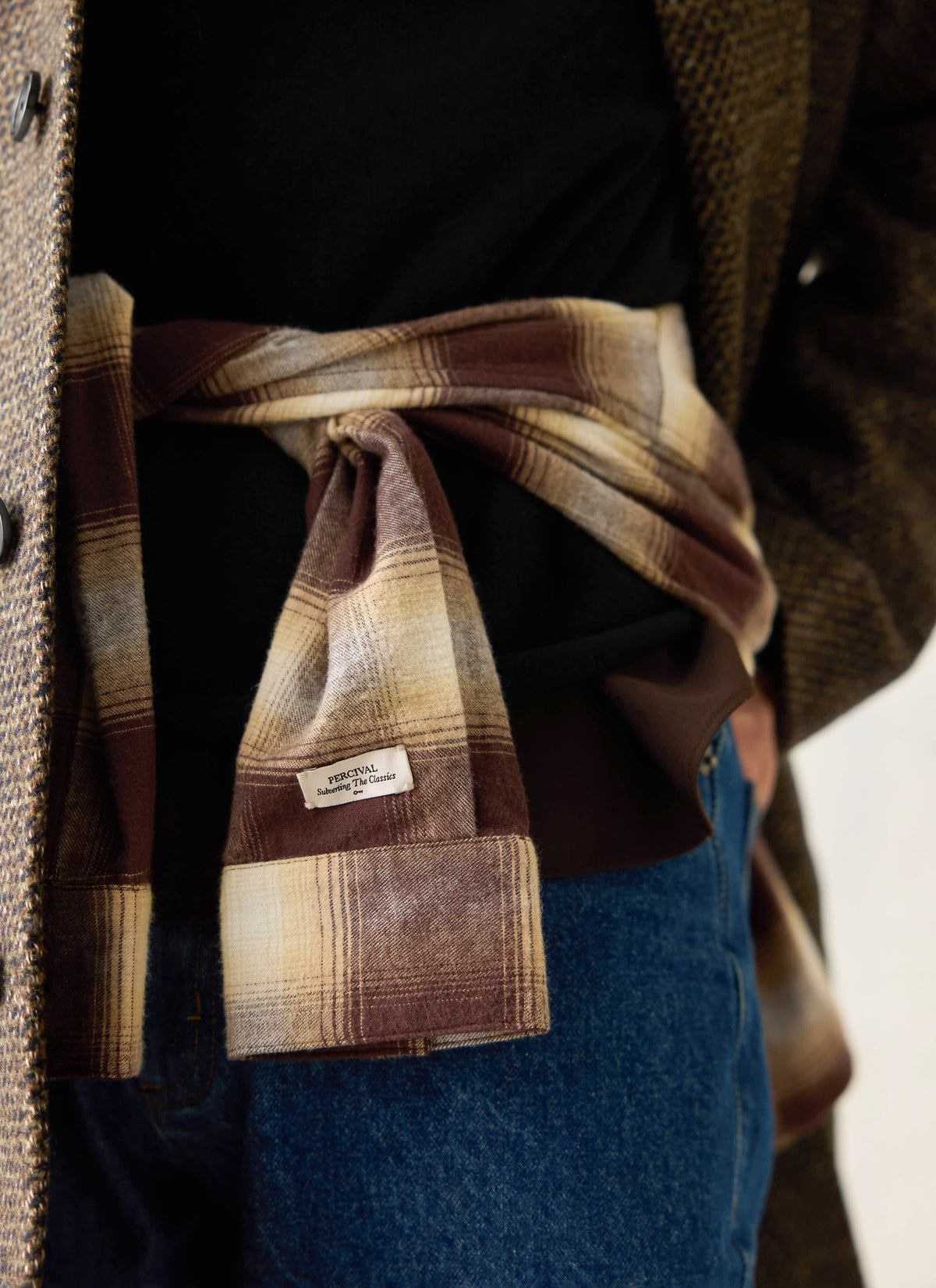 A model wearing the Percival brown checked cotton western shirt tied around the waist over a black top and jeans.