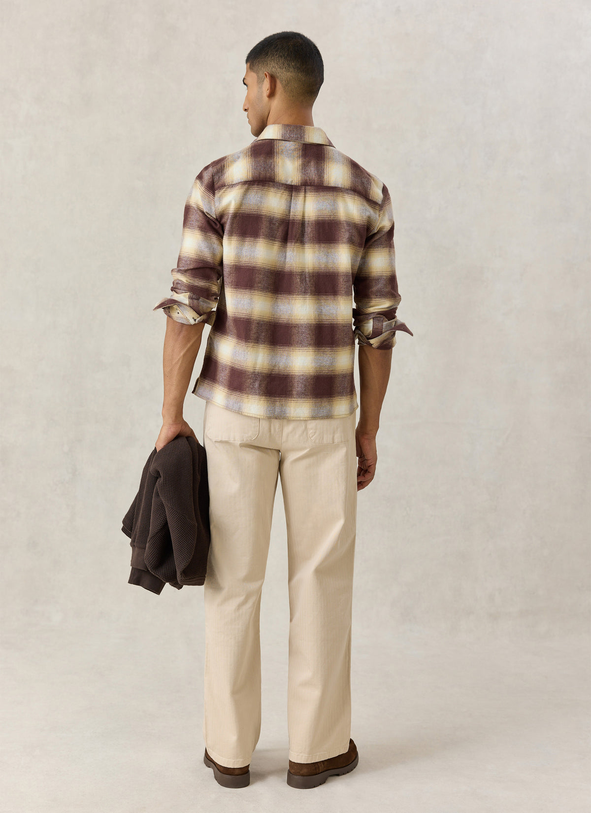 A model from the back wearing the Percival brown checked Ashe western shirt in 100% cotton with light trousers.