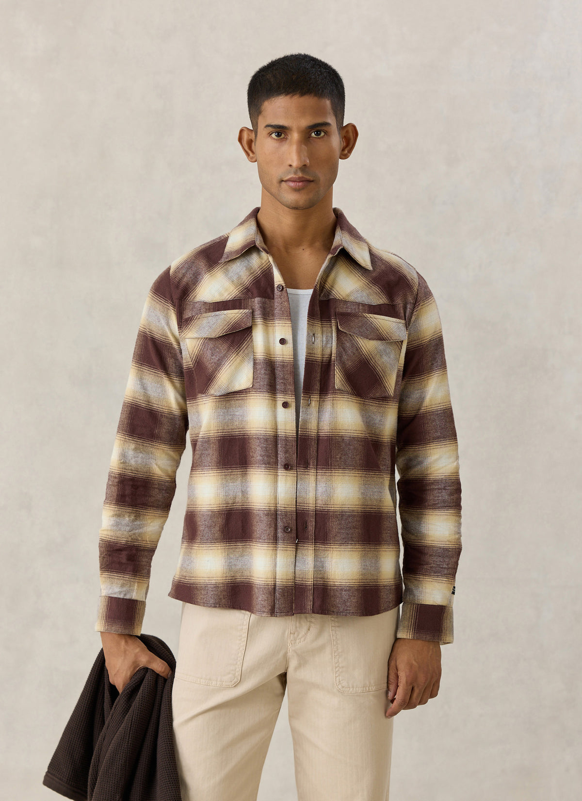 A model wearing the brown checked Percival Ashe cotton western shirt with dual pockets over a white tee and beige trousers.