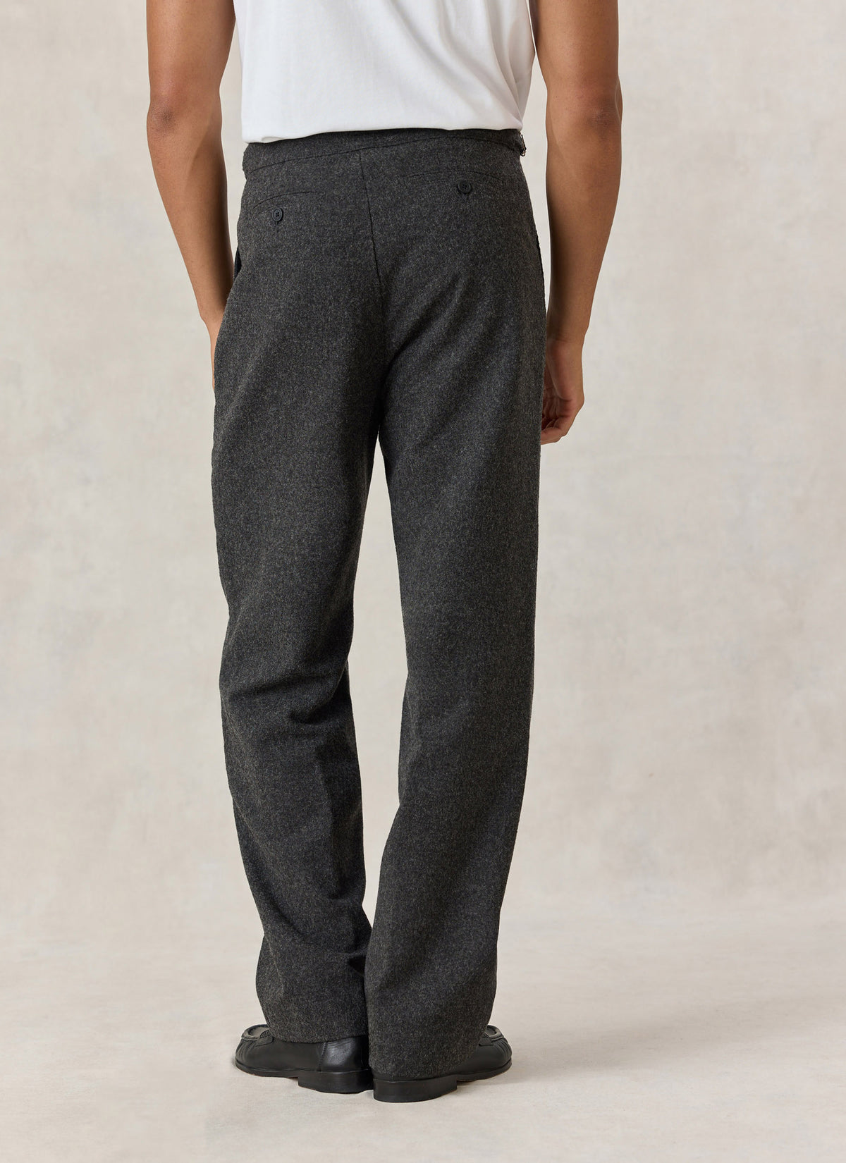 Rear view of a model wearing Percival Blake charcoal brushed-wool tailored trousers with a straight leg fit.