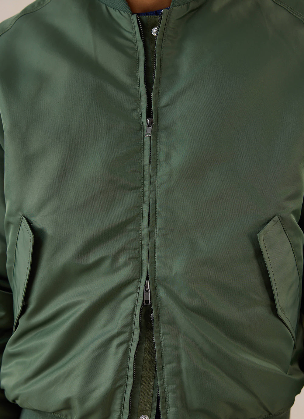 Close-up of the Percival forest green nylon bomber jacket showing the two-way zip and side pockets.