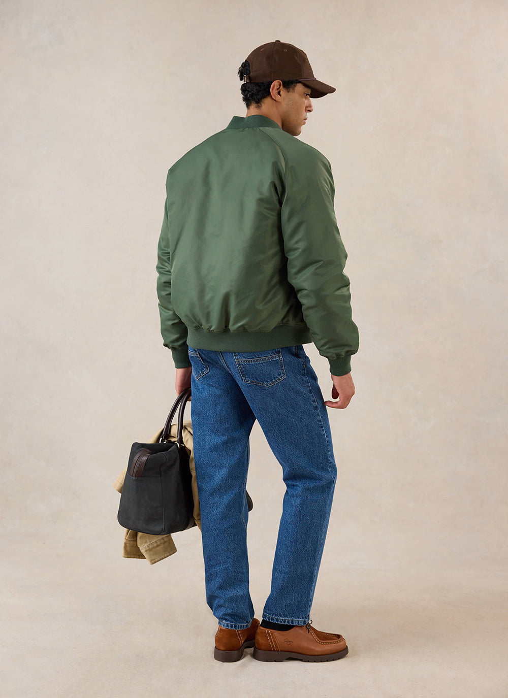 A model wearing the forest nylon bomber jacket from Percival with blue jeans, viewed from the back in a studio setting.