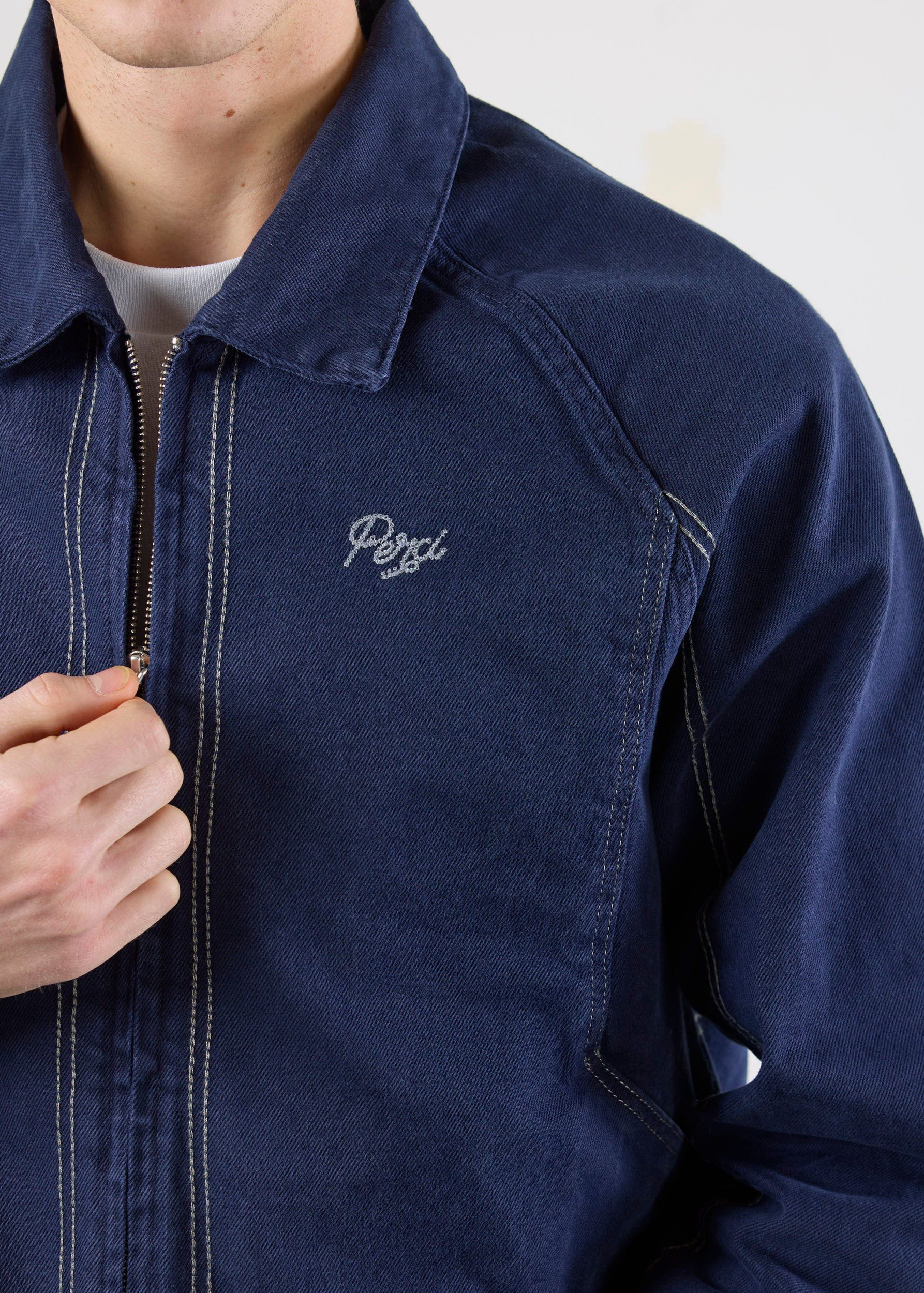 Close-up of the Percival Calabria Harrington jacket in navy cotton, showing the embroidered logo and contrast stitch.