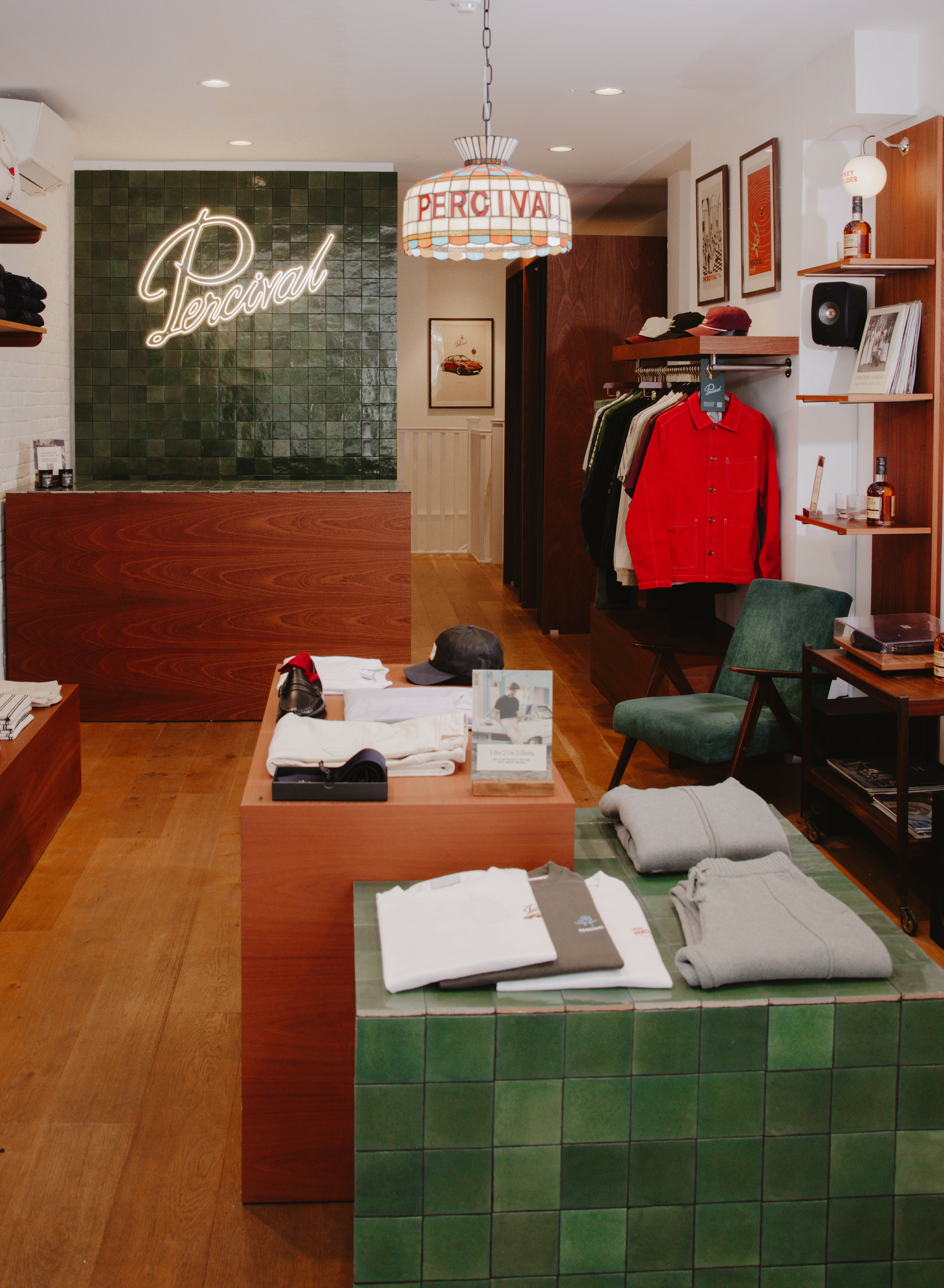 Inside the Percival store, showing clothing displays, a neon sign, and a framed art print on the back wall.