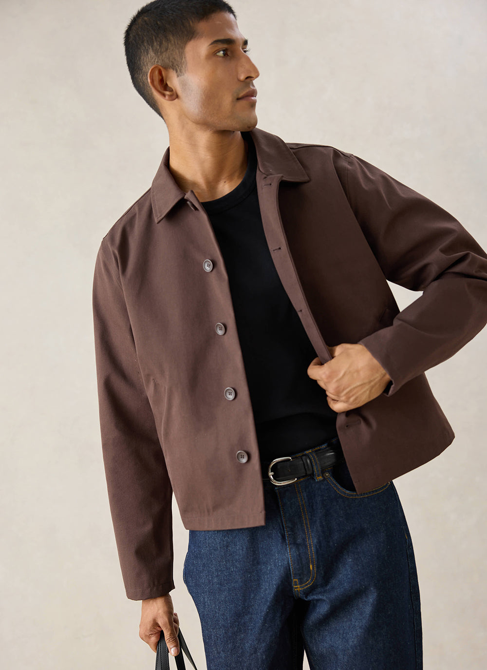 A model wears the espresso Percival Carter Cropped Jacket styled with a black t-shirt and blue jeans.