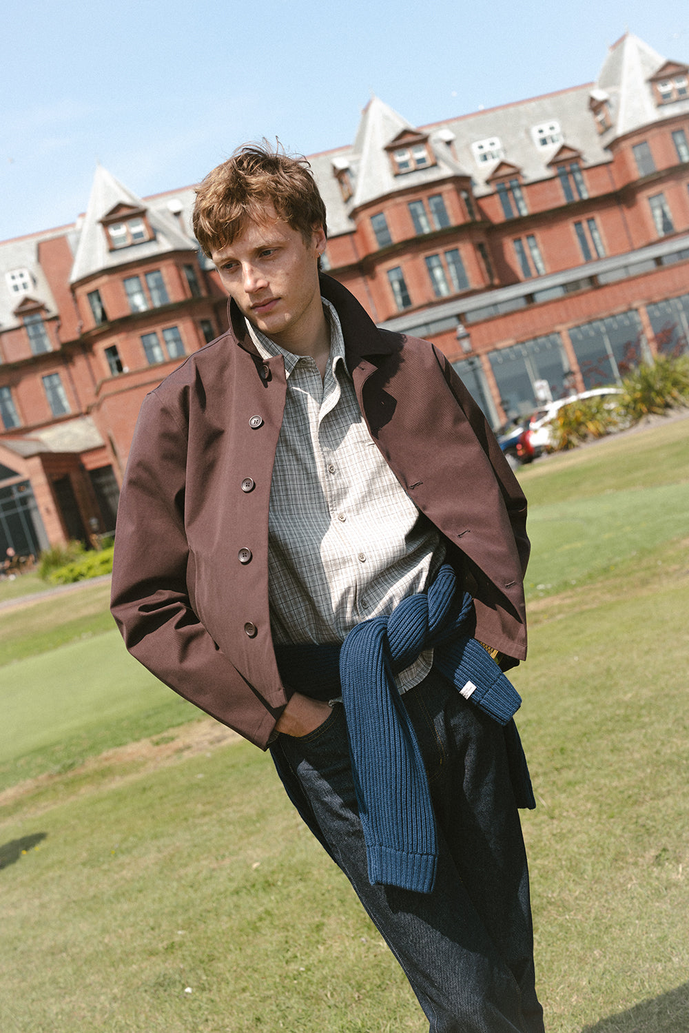 A model wears the Percival espresso brown Carter cropped trench coat with a cream check shirt, raw jeans, and a navy jumper.