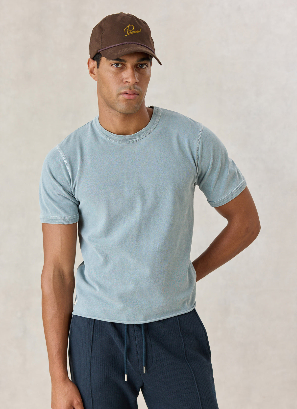 A model wearing the Percival light blue vintage wash cropped T-shirt in organic cotton and a brown cap.