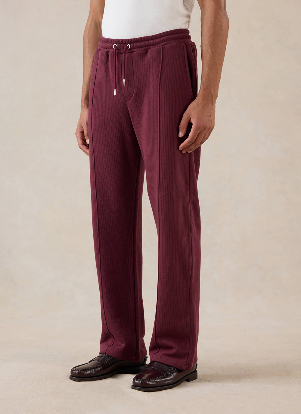 A model wears the merlot Percival Conrad Straight Leg Trackpants with a white t-shirt and loafers in a studio shot.