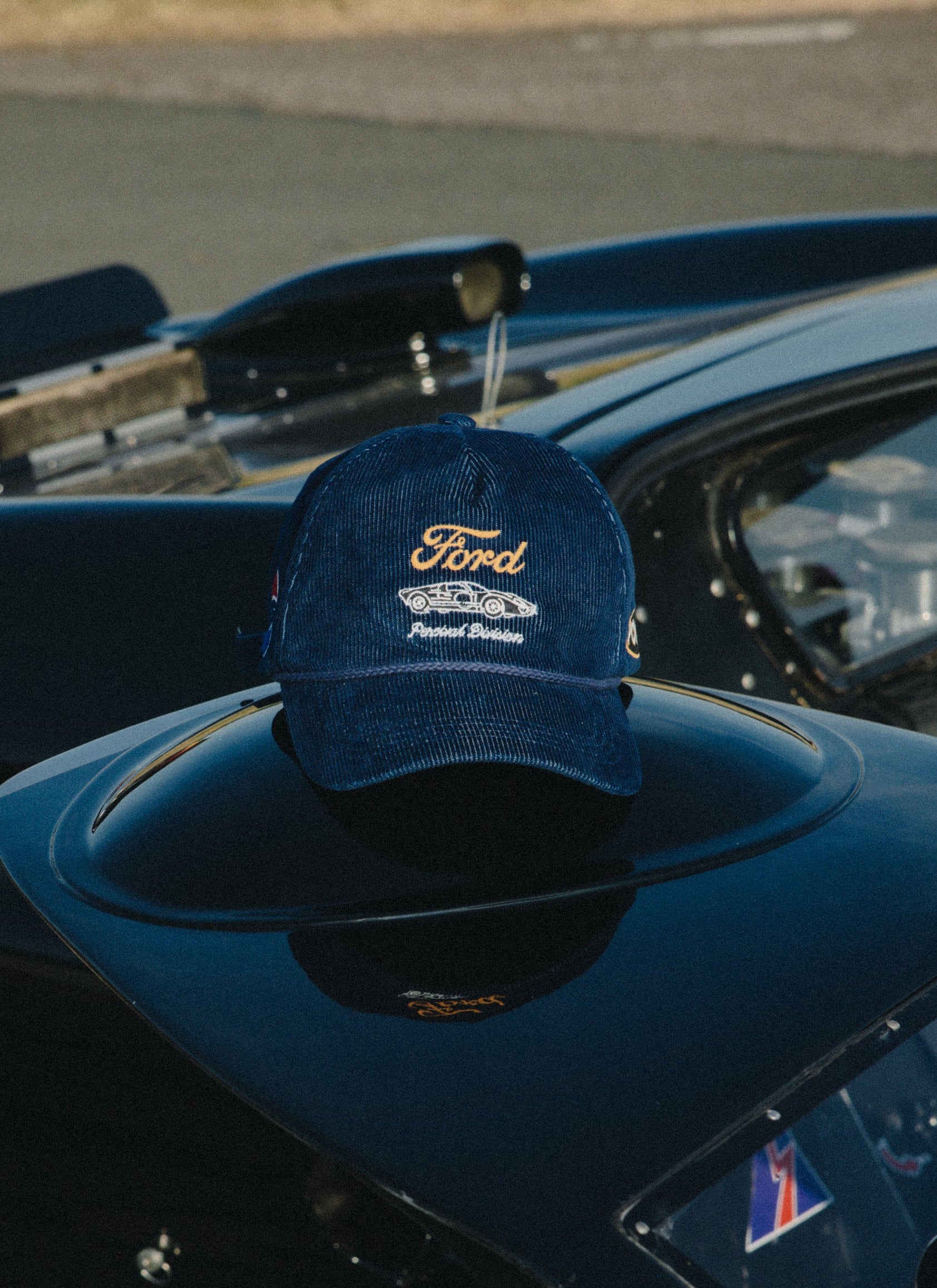 Navy corduroy Ford x Percival trucker cap with vintage embroidery, resting on a glossy black car exterior.