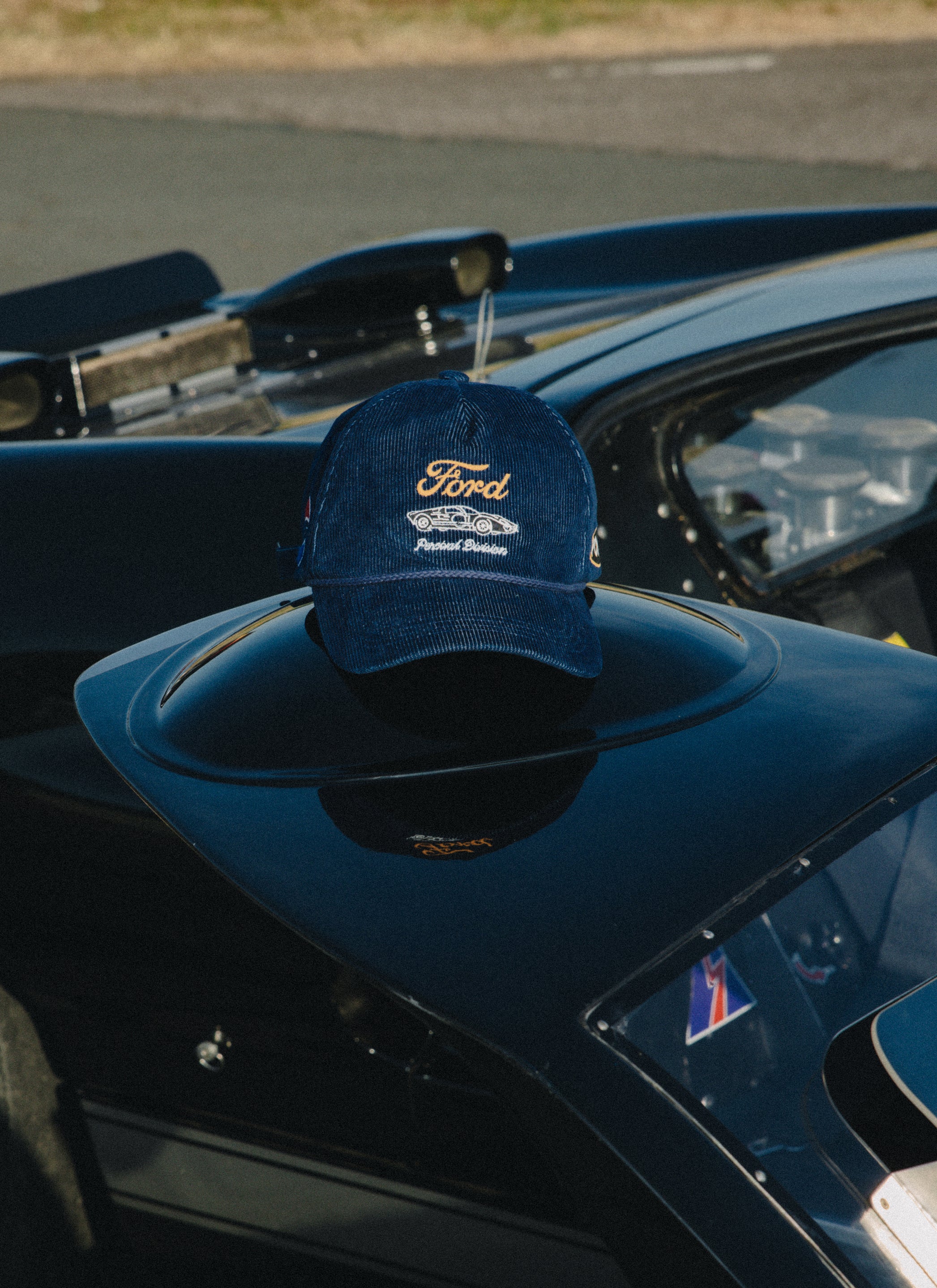 The navy corduroy Ford x Percival trucker cap with vintage car embroidery rests on a sleek classic race car.