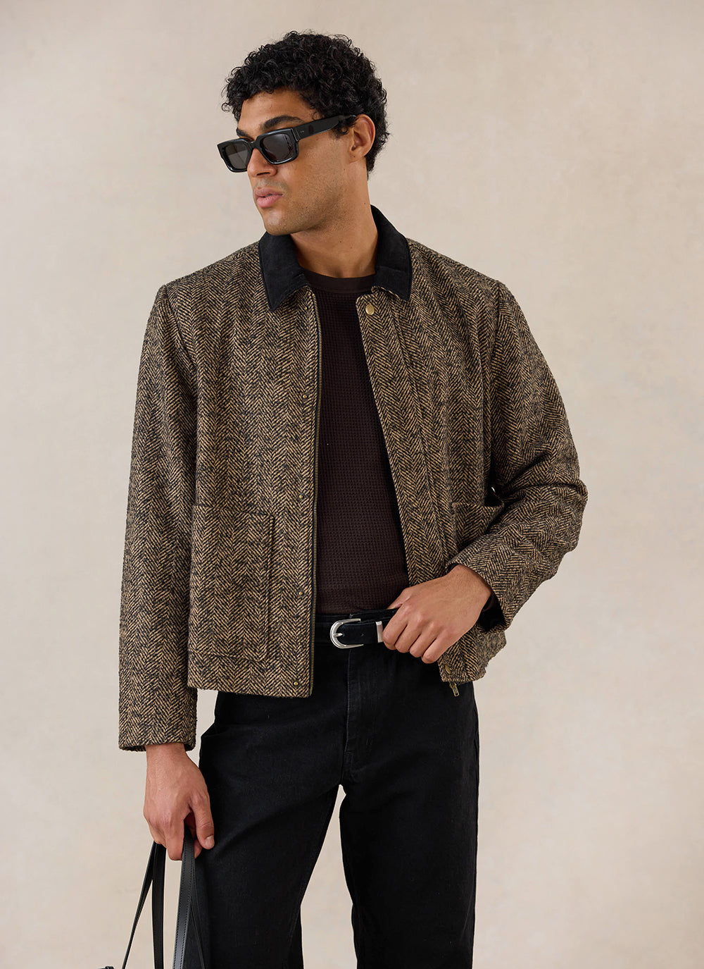 A model wears the brown herringbone wool Percival cropped boxy jacket with black trousers in a studio shot.