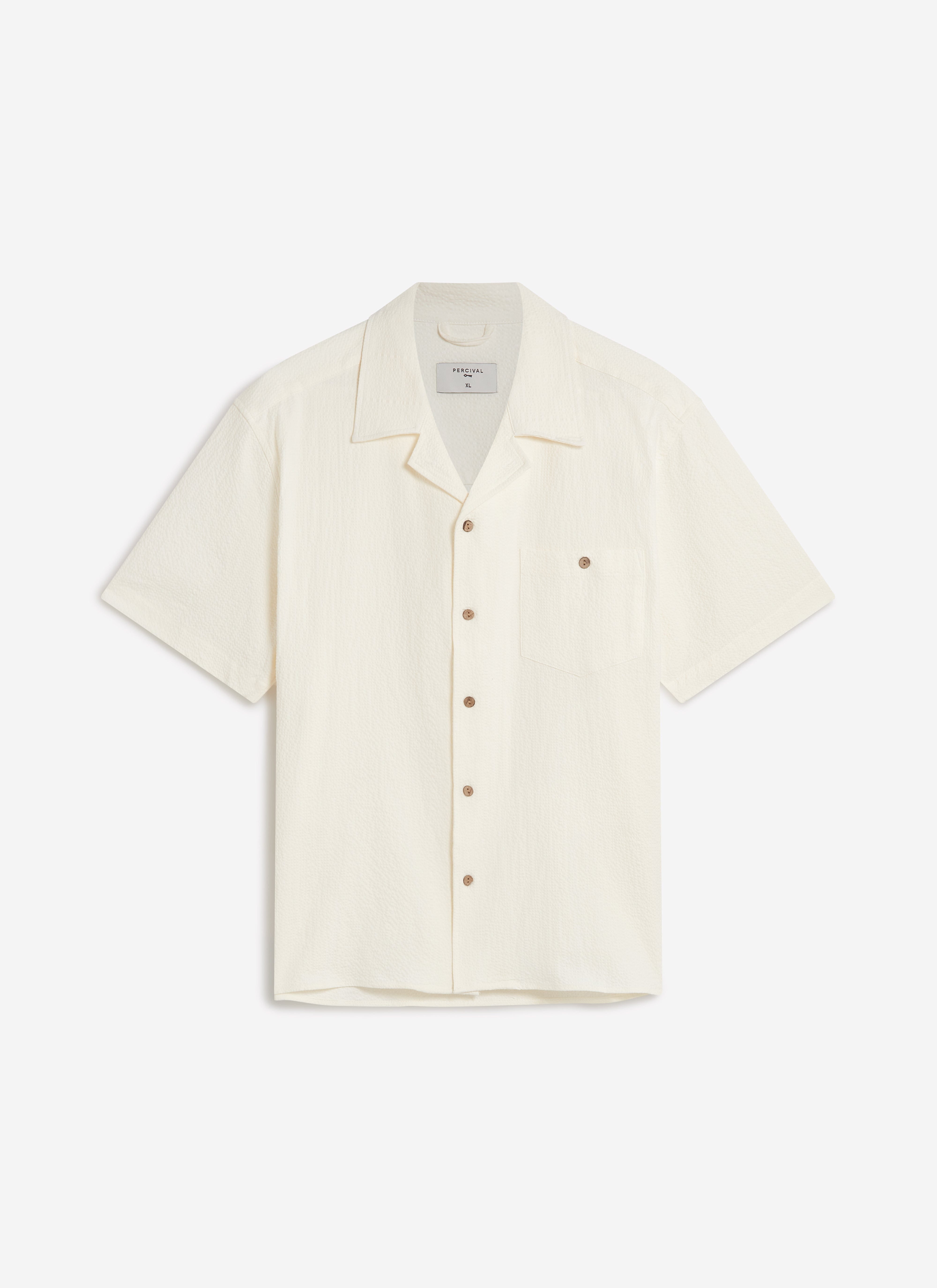 A flat lay of the Percival Cuban Shirt in ecru seersucker, showing the textured fabric, Cuban collar and chest pocket.