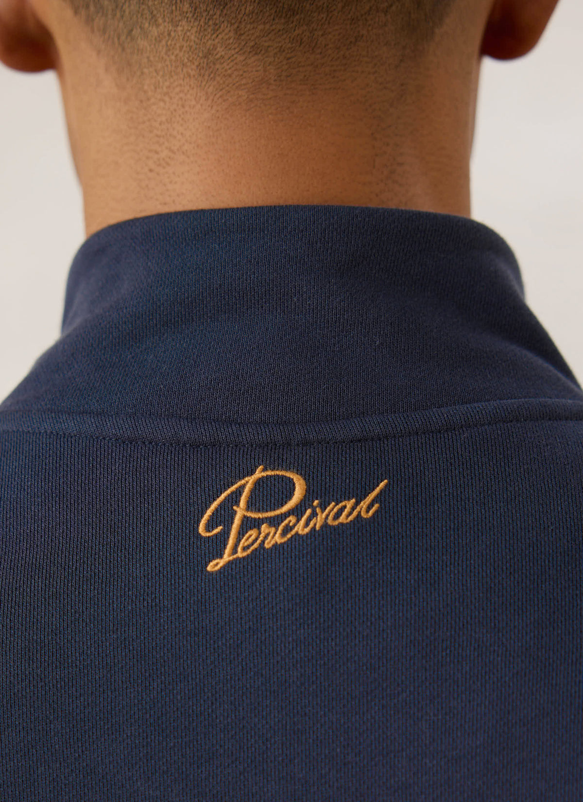 Close-up of the back neck showing the embroidered Percival logo on the navy blue Curtis funnel neck zip up sweatshirt.