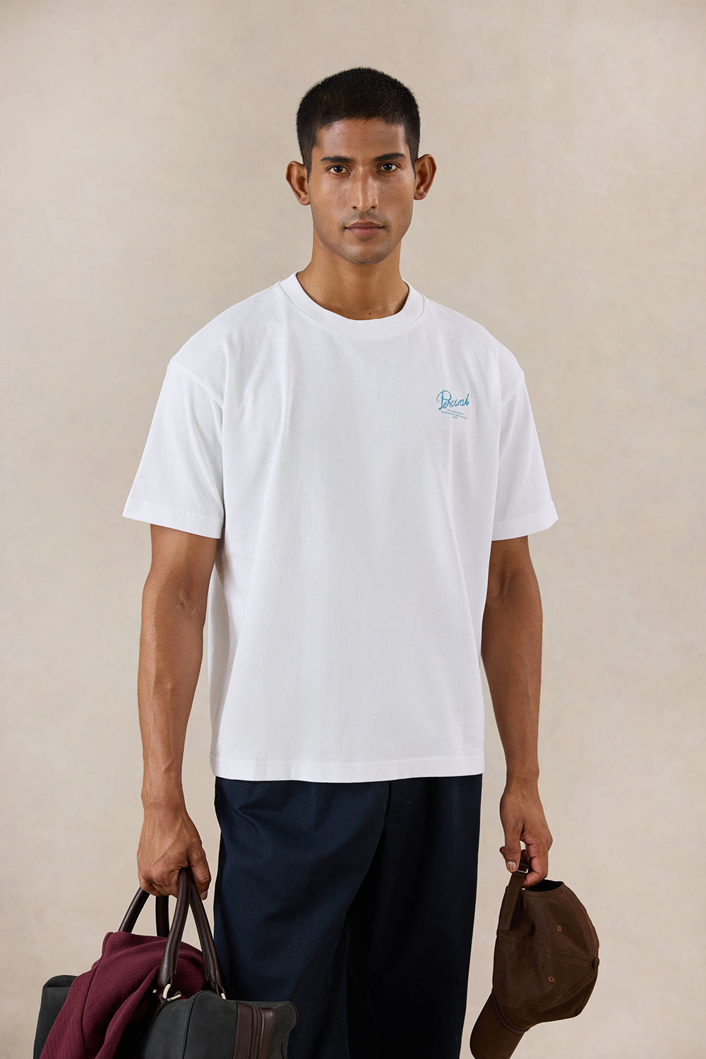 A model wears the white Percival Dawson boxy t-shirt, styled with dark trousers and accessories in a studio setting.