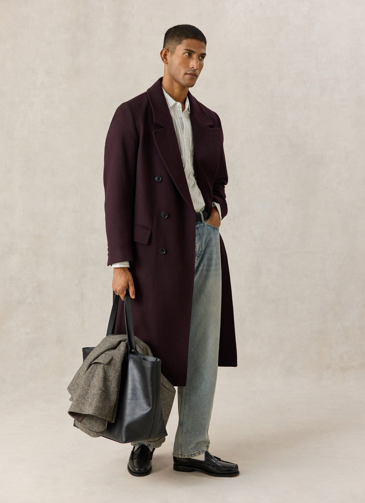 Model wearing the Percival dark brown wool-blend double-breasted overcoat, light jeans, and holding a black leather tote bag.