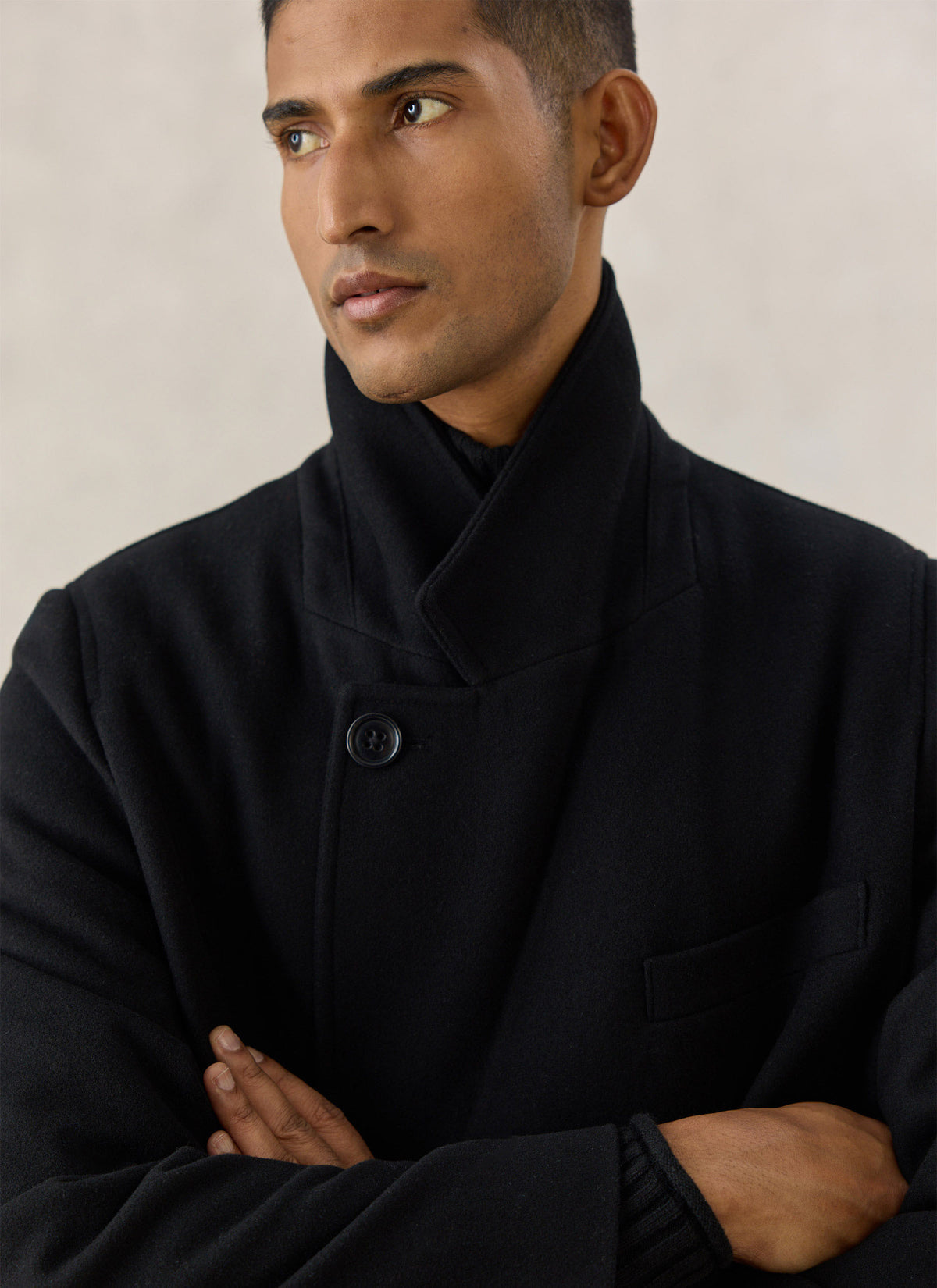 Close-up of a model wearing Percival's black double-breasted wool blend overcoat with a high collar and button fastening.