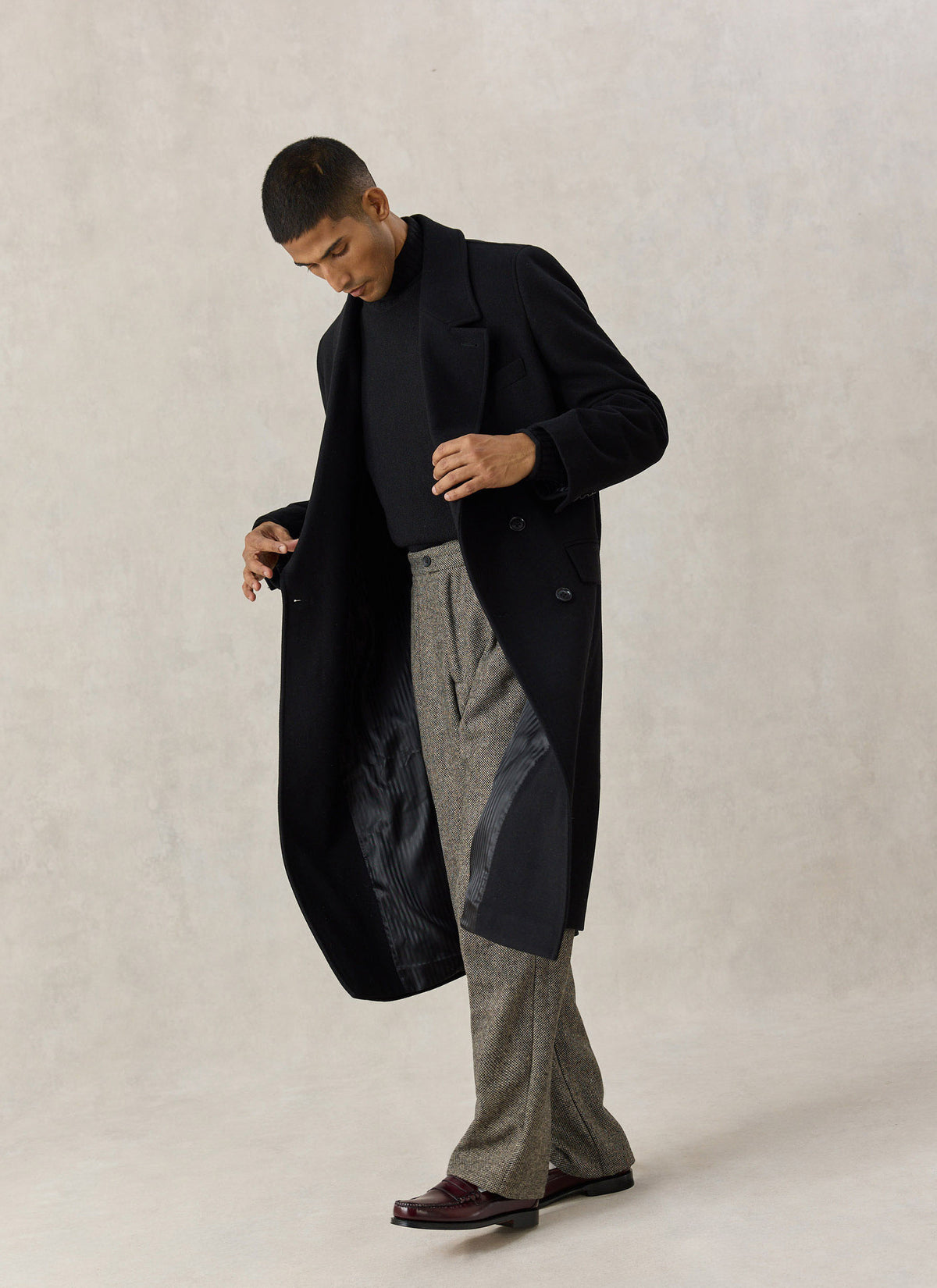 A model wearing the Percival black wool blend double-breasted overcoat with patterned trousers and loafers.