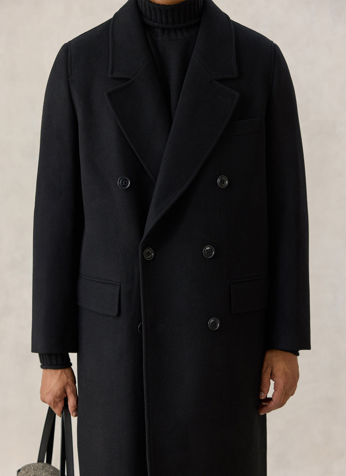 A model wearing a black wool blend double-breasted overcoat from Percival, showing wide lapels and button details.