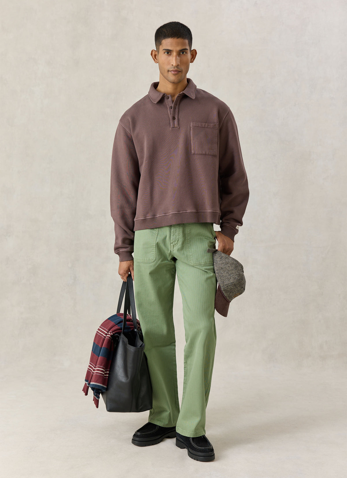 Model wearing the brown Percival Dudley vintage wash popover sweatshirt with green trousers and a black leather bag.