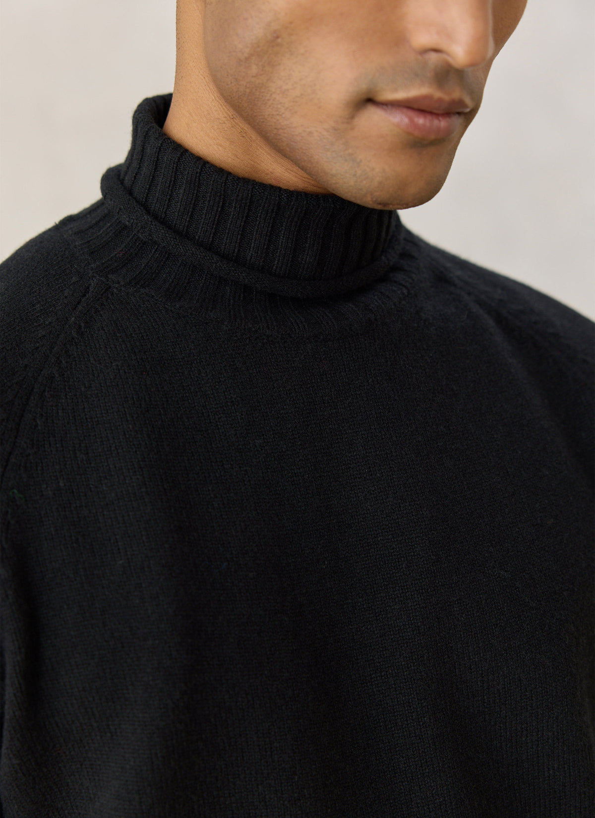 A close-up of the Percival black wool Dylan roll neck jumper, highlighting the ribbed collar and raglan sleeves.