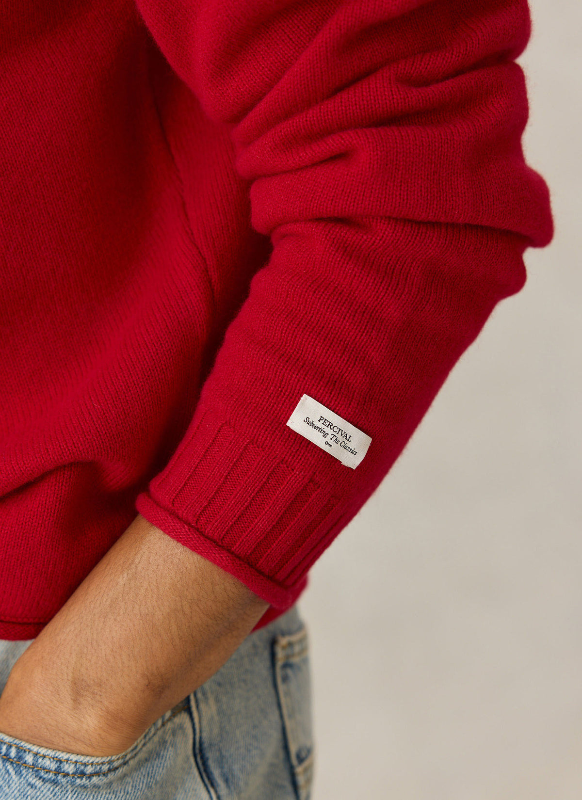 A close-up of the Percival Dylan red wool jumper sleeve, highlighting the ribbed cuff and branded label.