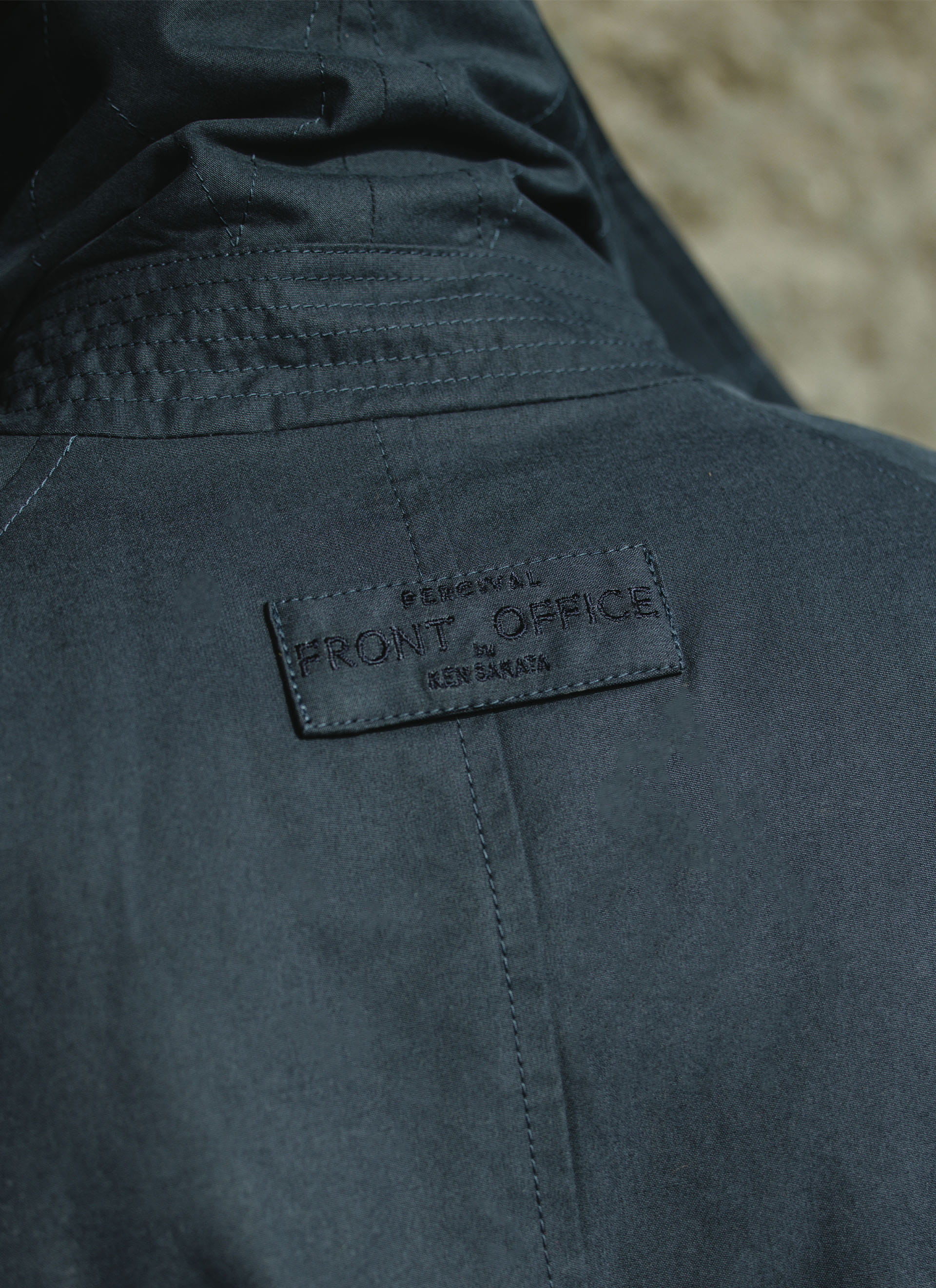 Close-up of the embroidered Front Office x Percival collab label on the back of the navy peached cotton Mac Coat.