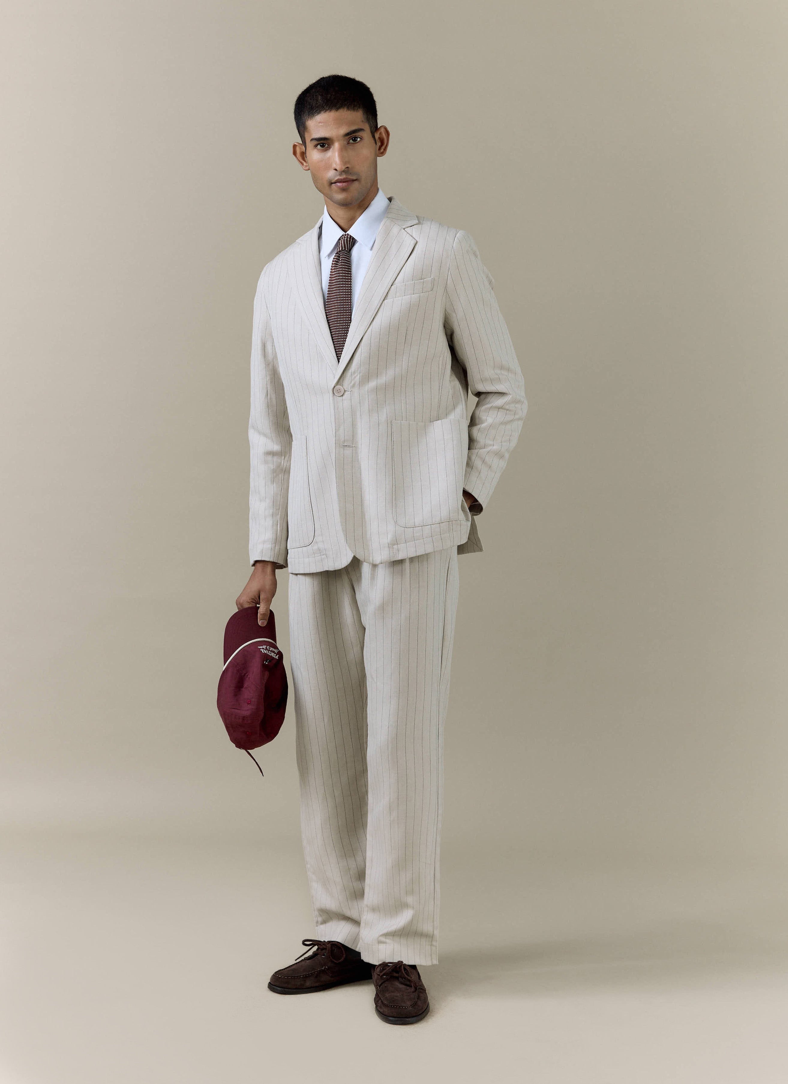 A model wears the Percival cream striped tailored linen-blend blazer and matching trousers in a studio setting.