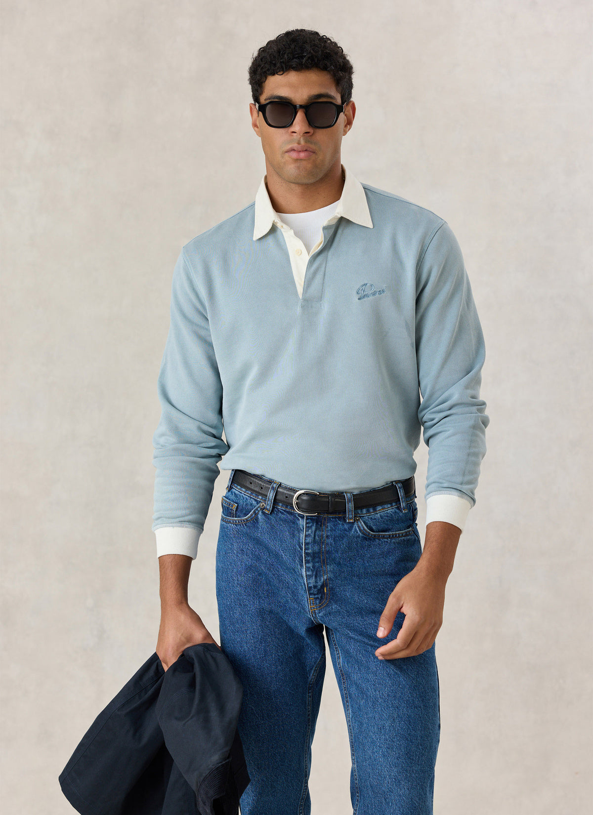 A model wearing the light blue Percival cotton rugby polo shirt with a contrasting cream collar, blue jeans, and sunglasses.
