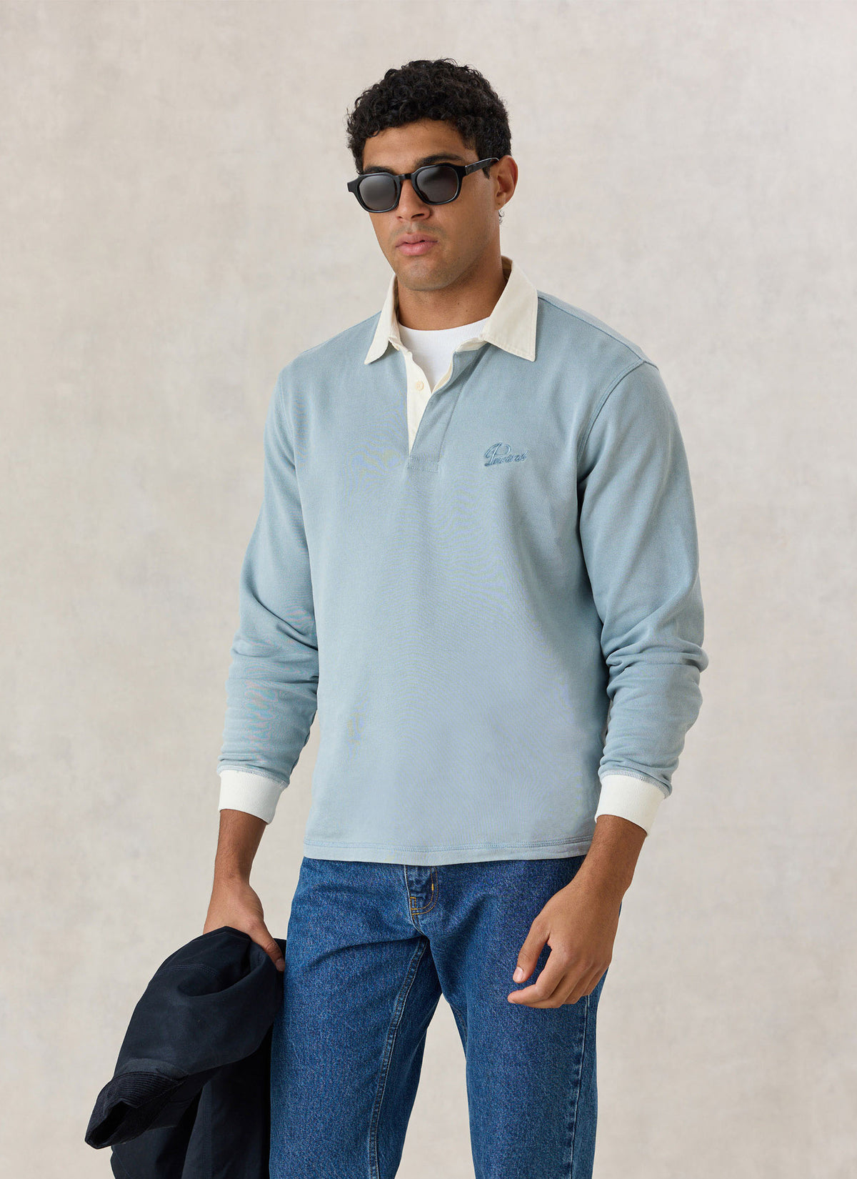 A model wearing the light blue Percival rugby polo shirt with a contrasting cream collar and blue jeans.