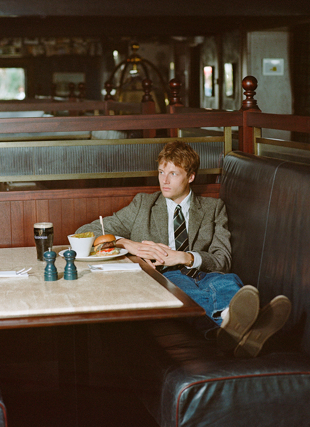 A model wears a Percival multi stripe silk tie with a striped shirt and brown blazer, sitting in a pub booth.