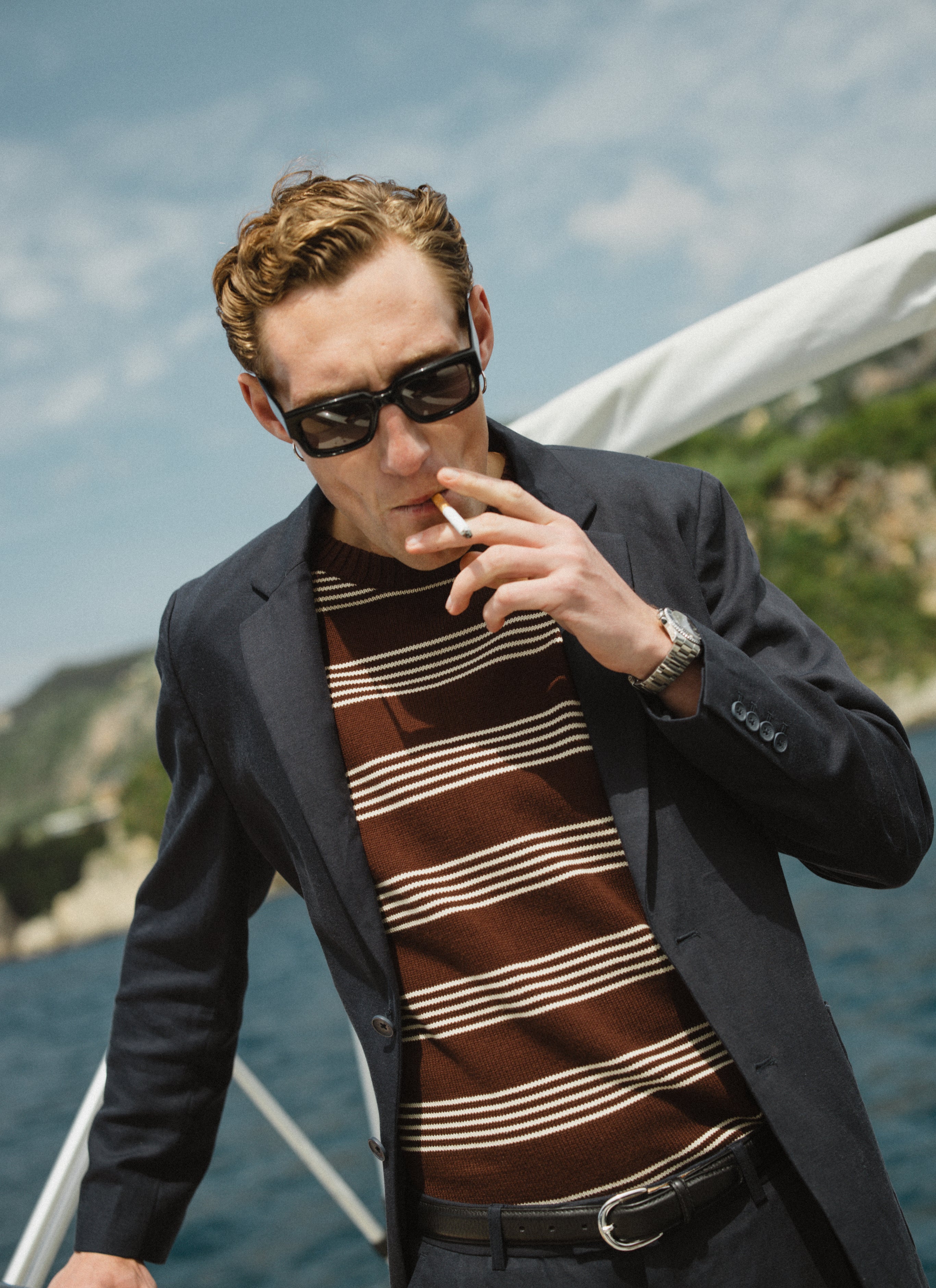 The Percival Fiction Knitted T-Shirt in espresso brown with ecru stripes, layered under a blazer on a boat.