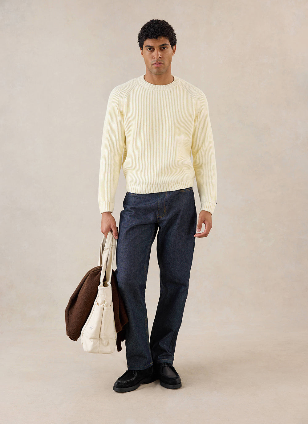 A model wears the cream Percival Fisherman knitted jumper, styled with dark jeans and holding a canvas tote bag.