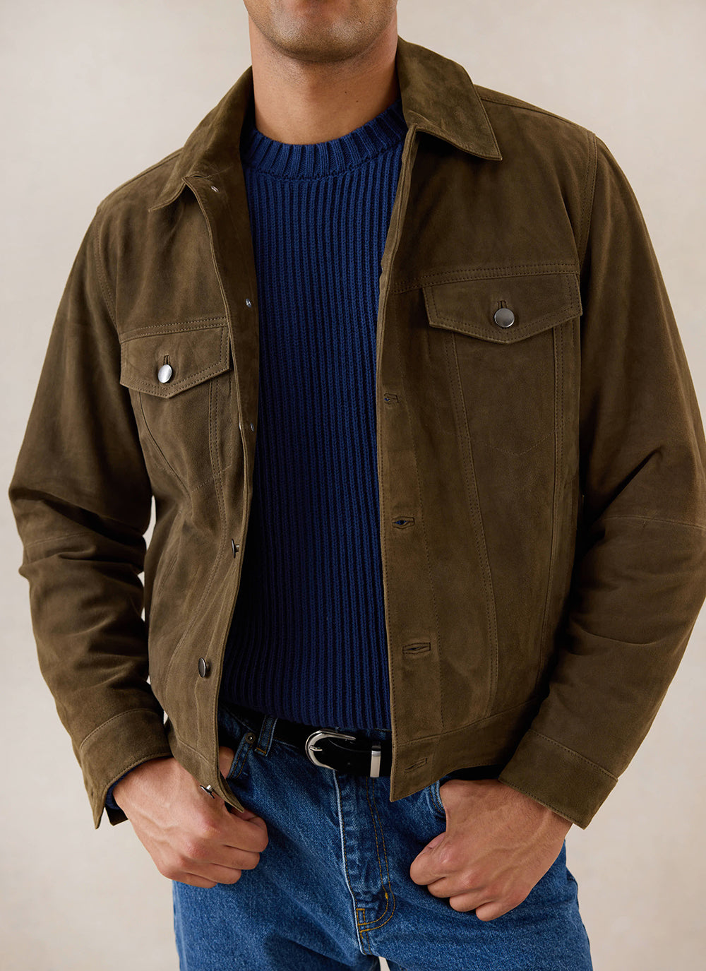 A model wears the navy Percival fisherman knitted jumper under an olive jacket and blue jeans.
