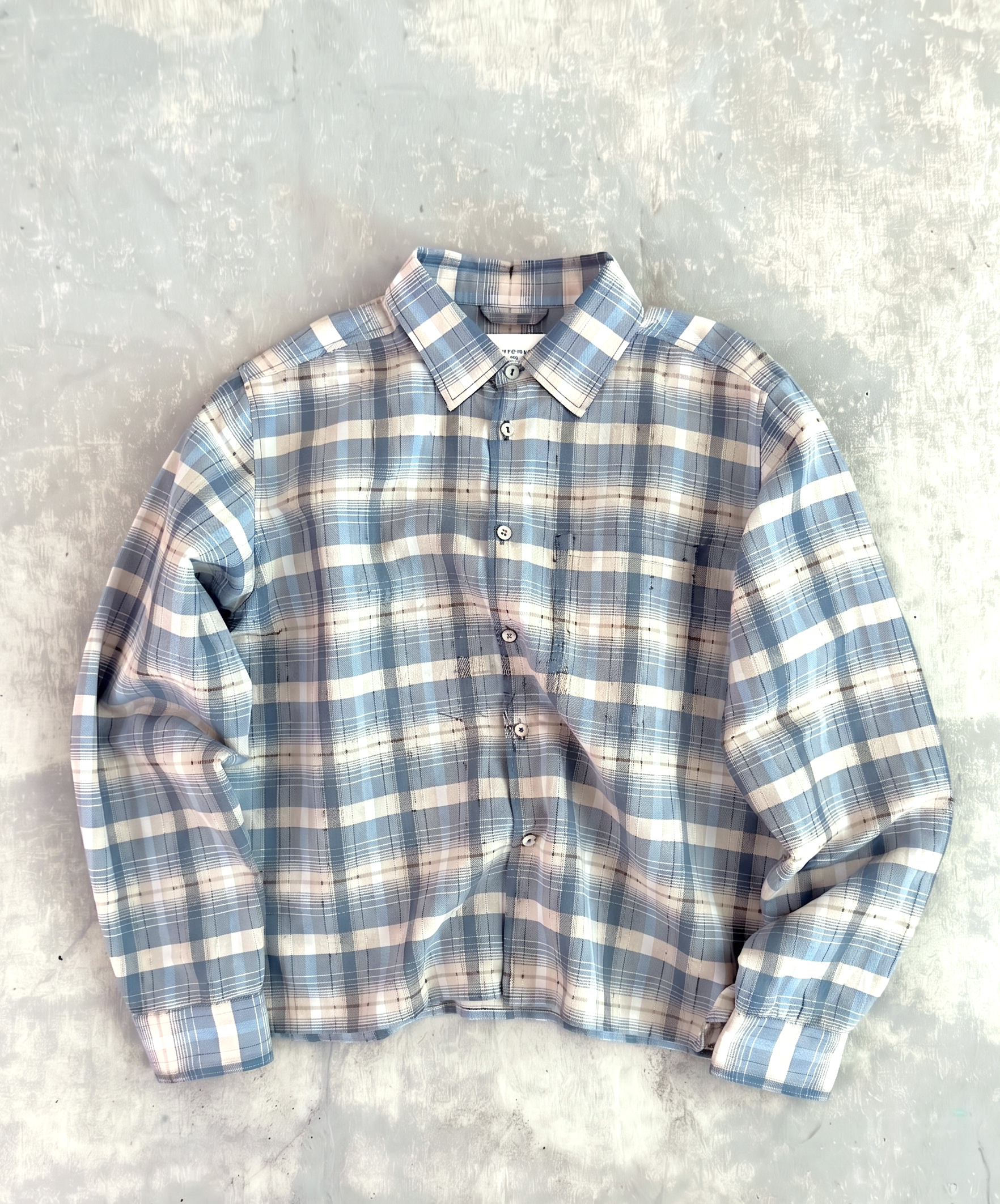 Percival Jesse cropped shirt in light blue check linen-cotton blend, shown in a flat-lay against a textured background.