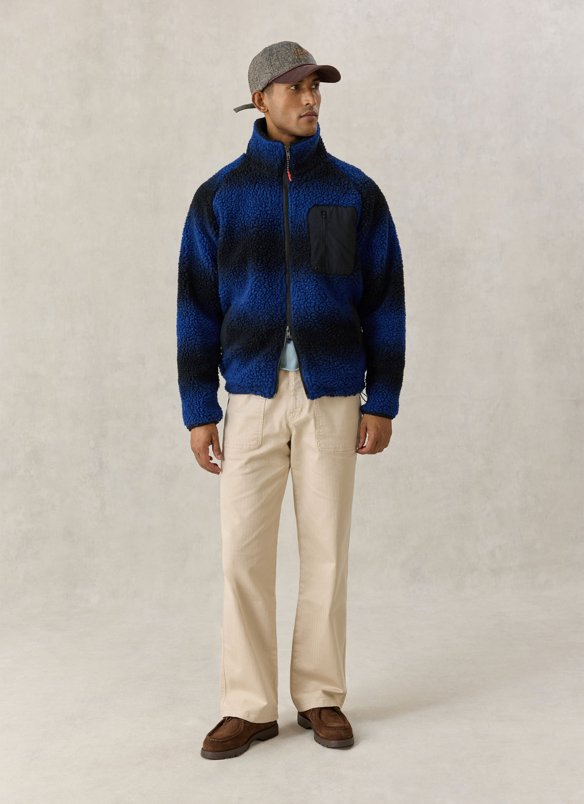 A model wearing the Percival ombre blue fleece jacket with a stand collar, paired with beige trousers and a cap.