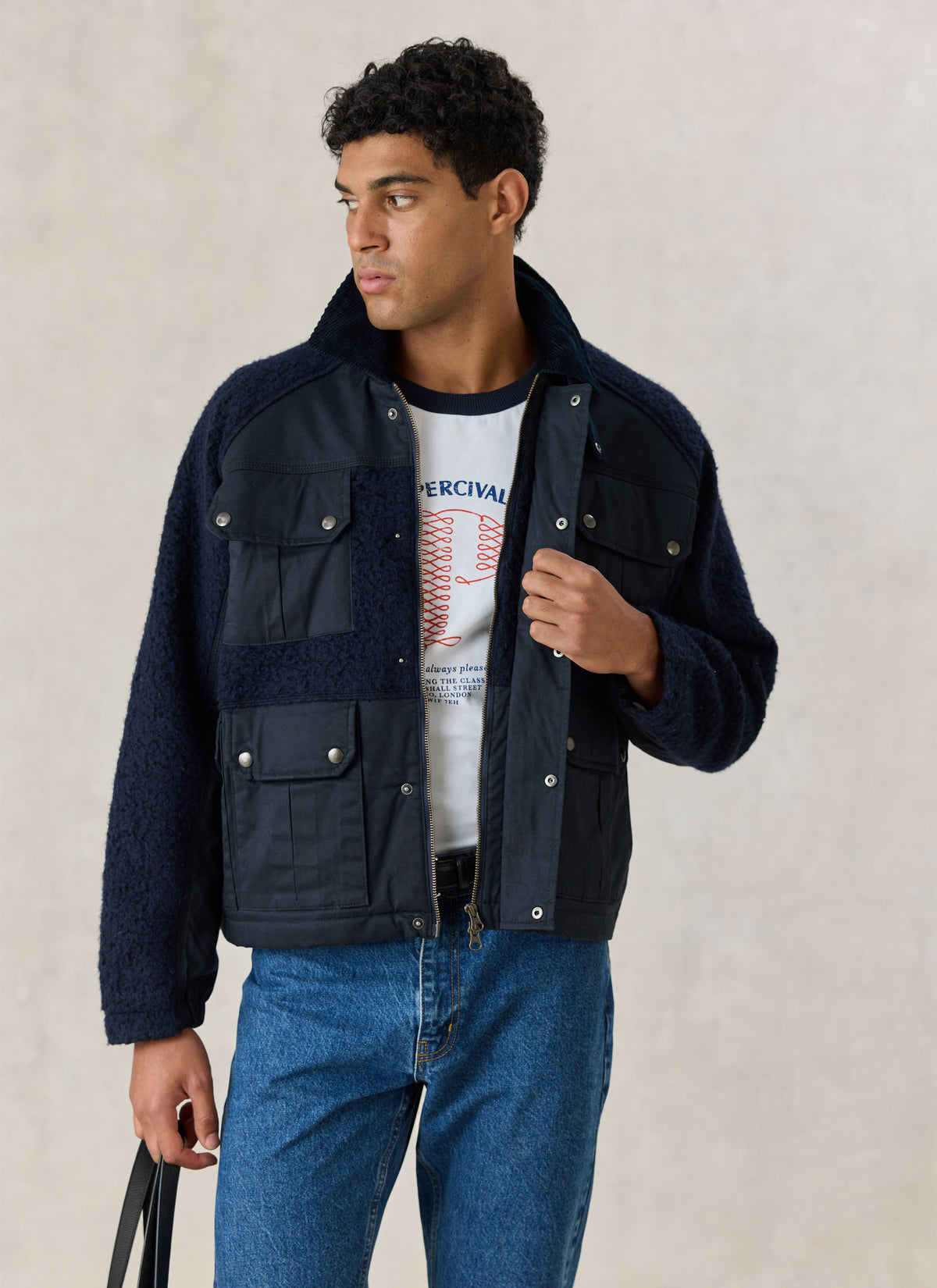 A model wearing the navy Fletcher utility fleece and wax jacket with multiple pockets over a white graphic t-shirt and jeans.